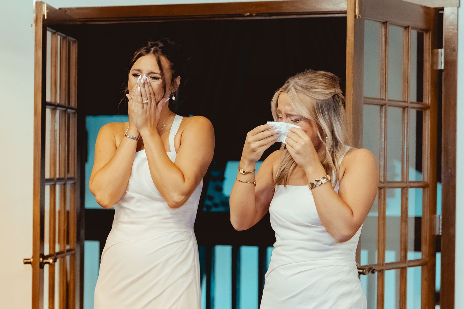 Two emotional brides in white dresses crying tears of joy during their wedding first look moment.