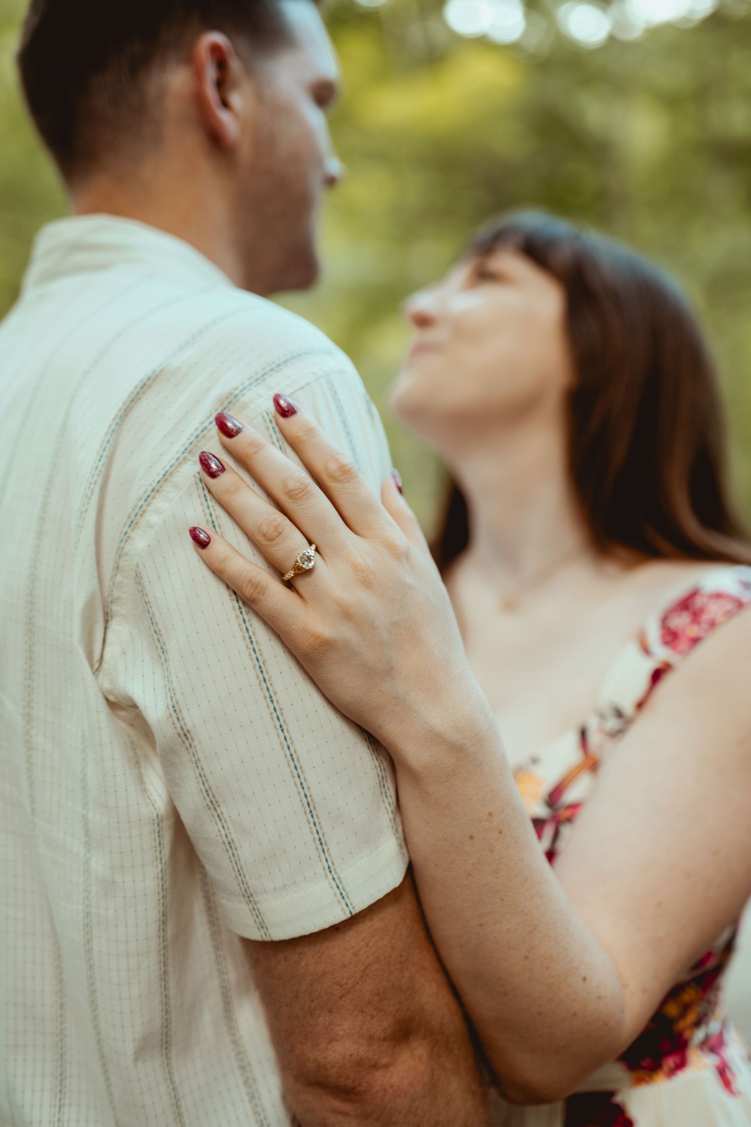 Close-up of a woman's hand with an engagement ring resting on a man's arm during an outdoor couples photo session.