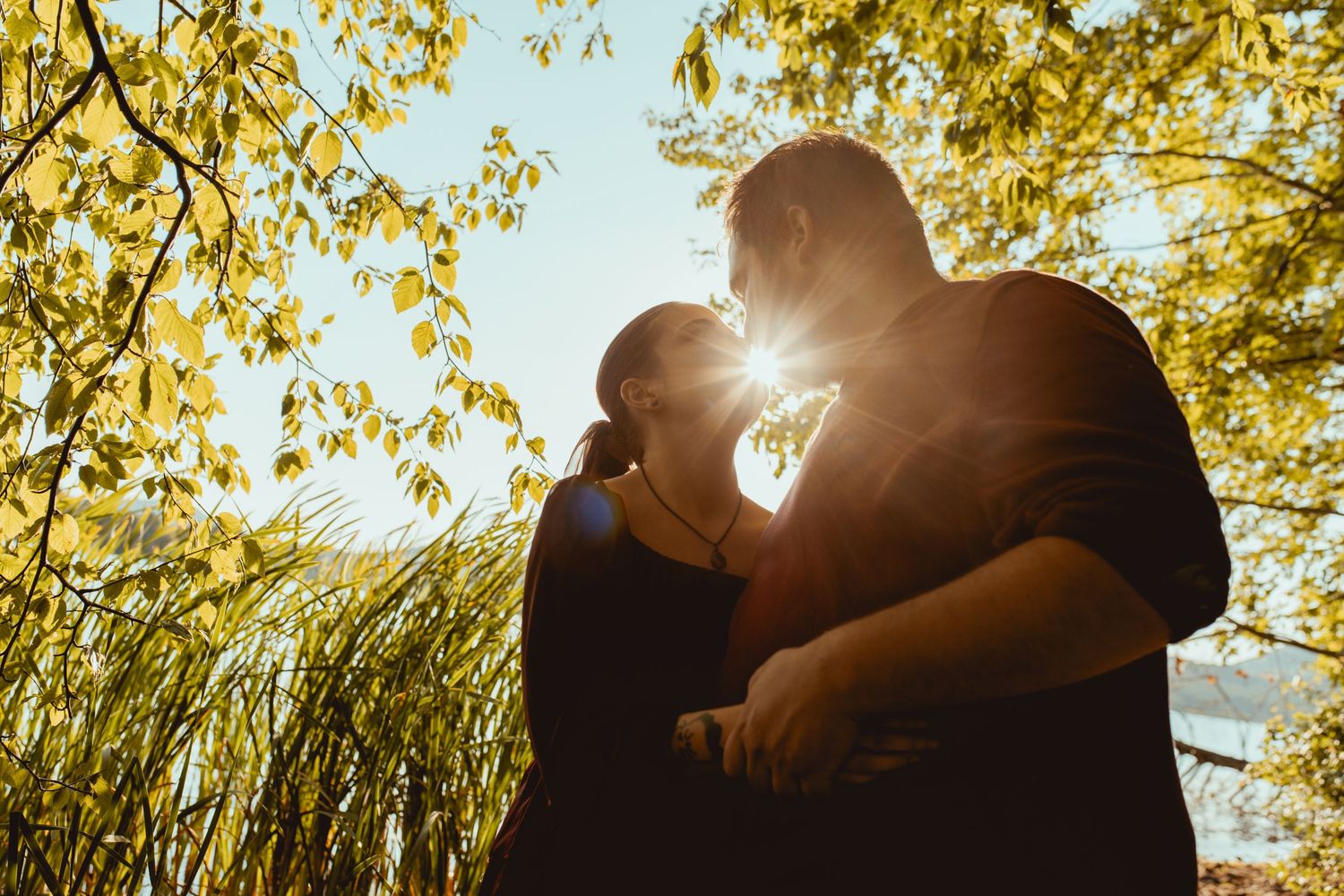 A romantic silhouette of a couple embracing under golden autumn trees with sunlight streaming through the branches.