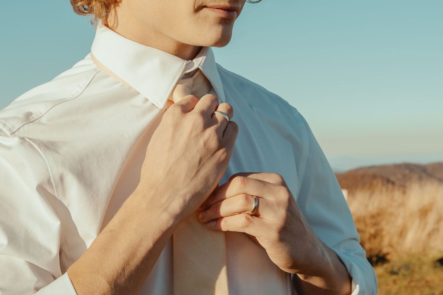 Person in a white shirt poses against a desert landscape with mountains in the background during golden hour.