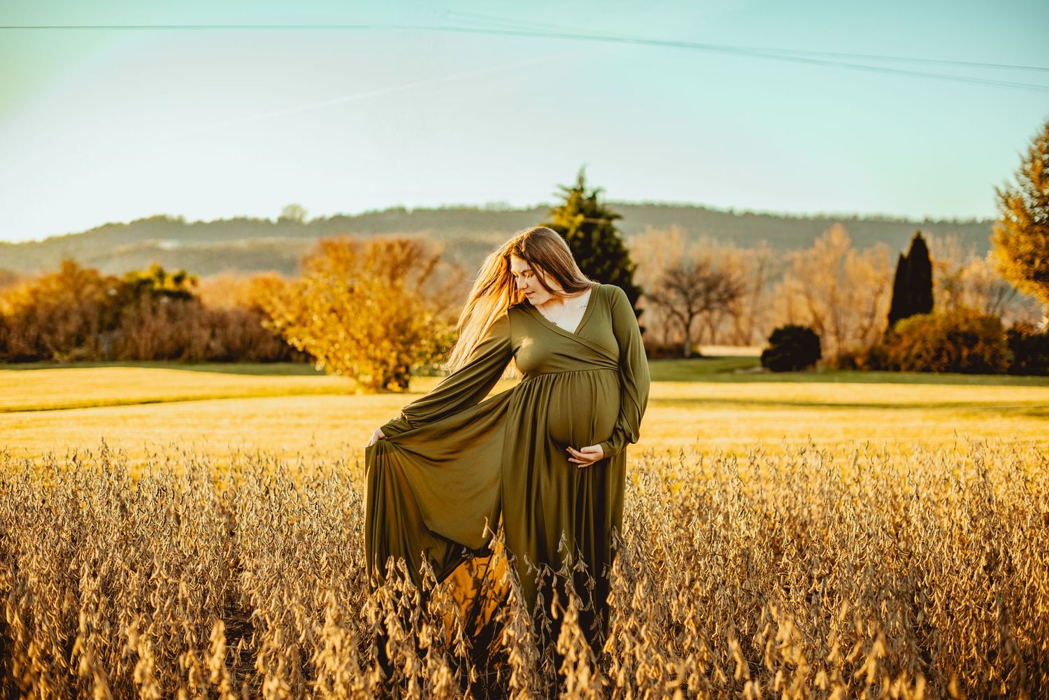 Two figures in dark cloaks stand together in a golden autumn cornfield at sunset.