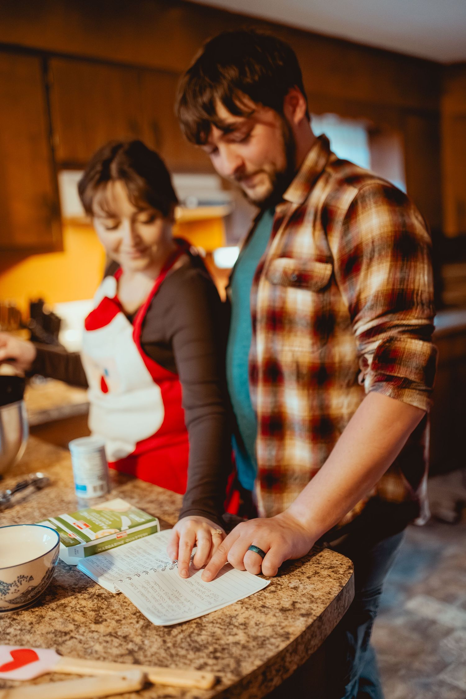 Two people working together at a kitchen counter with a granite surface in warm lighting.