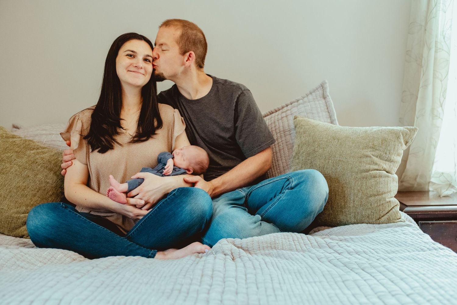 A couple sits cross-legged on a bed with pillows, sharing an intimate moment together.