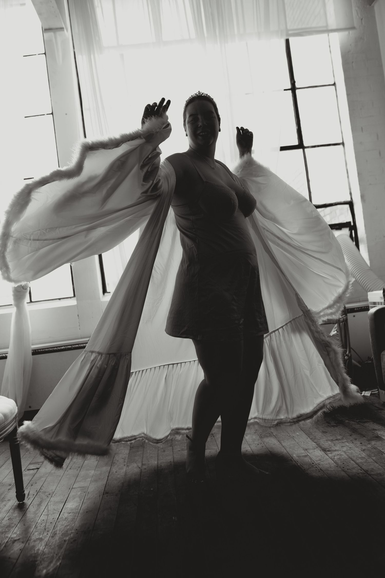 Black and white photograph of dancers in flowing white dresses performing a dynamic movement sequence on a wooden floor.