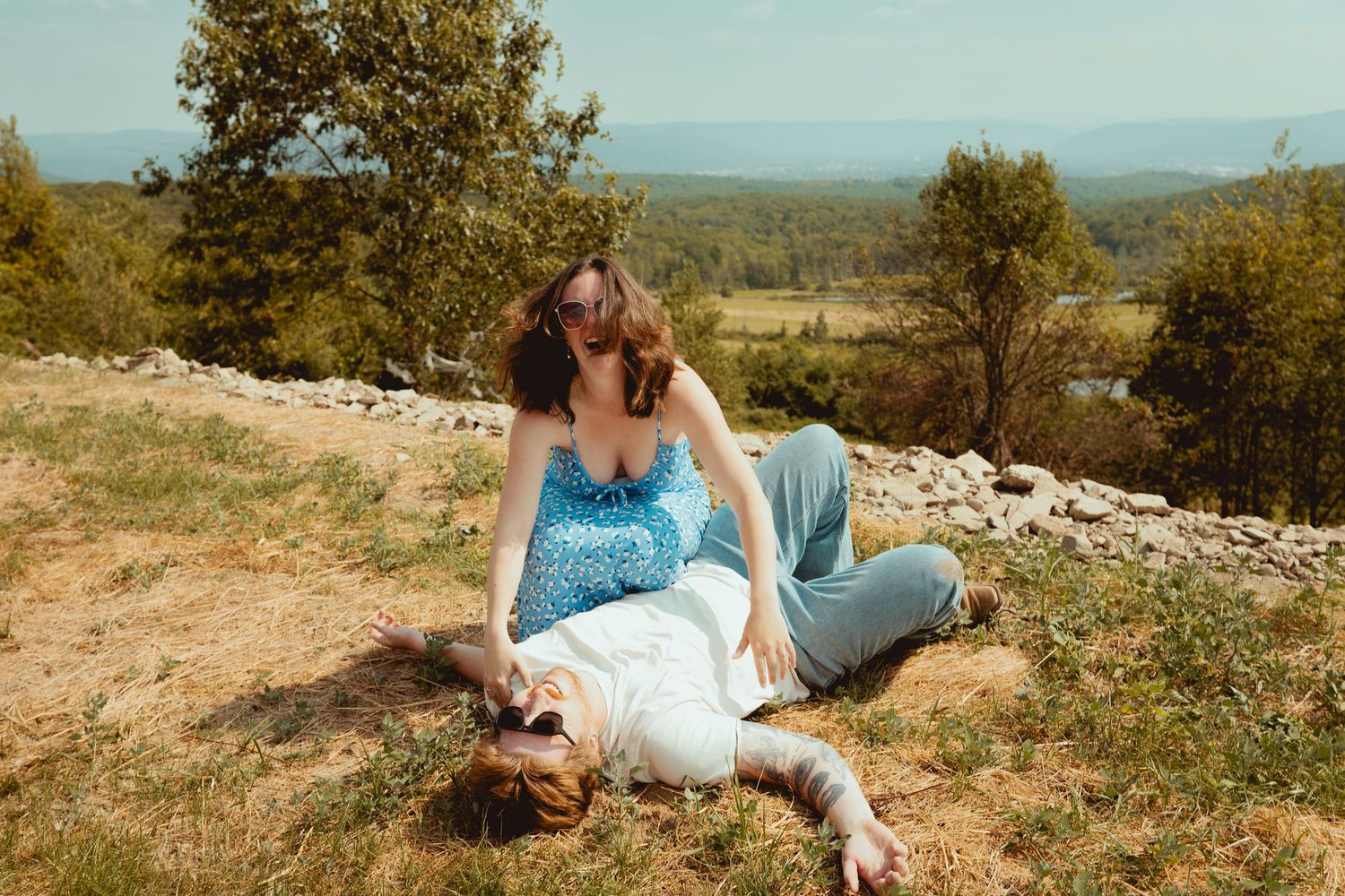 A series of dreamy outdoor photos showing someone in a white dress lounging in a grassy hilltop meadow at sunset.