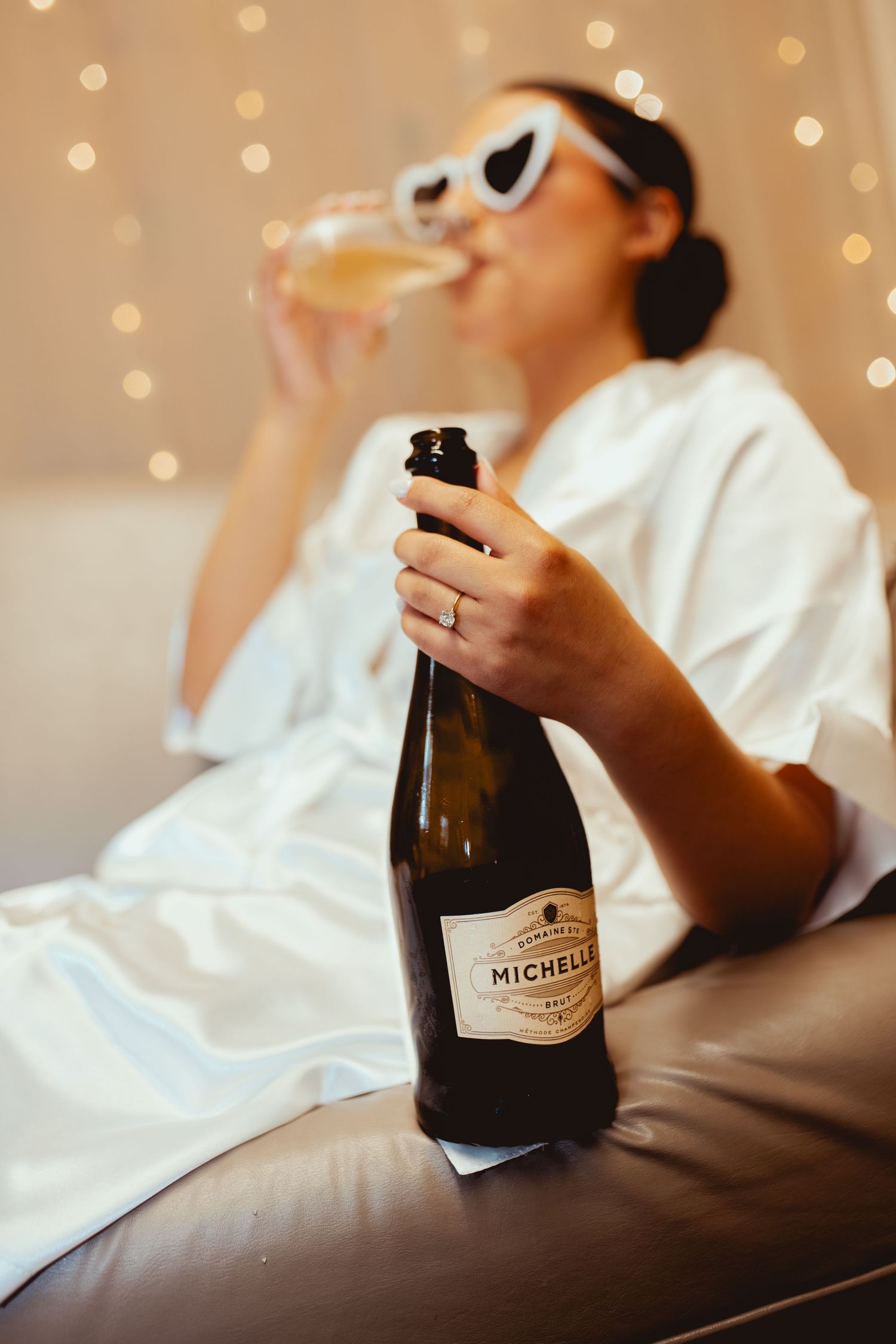 Champagne bottle being held against a white background with soft bokeh lights.