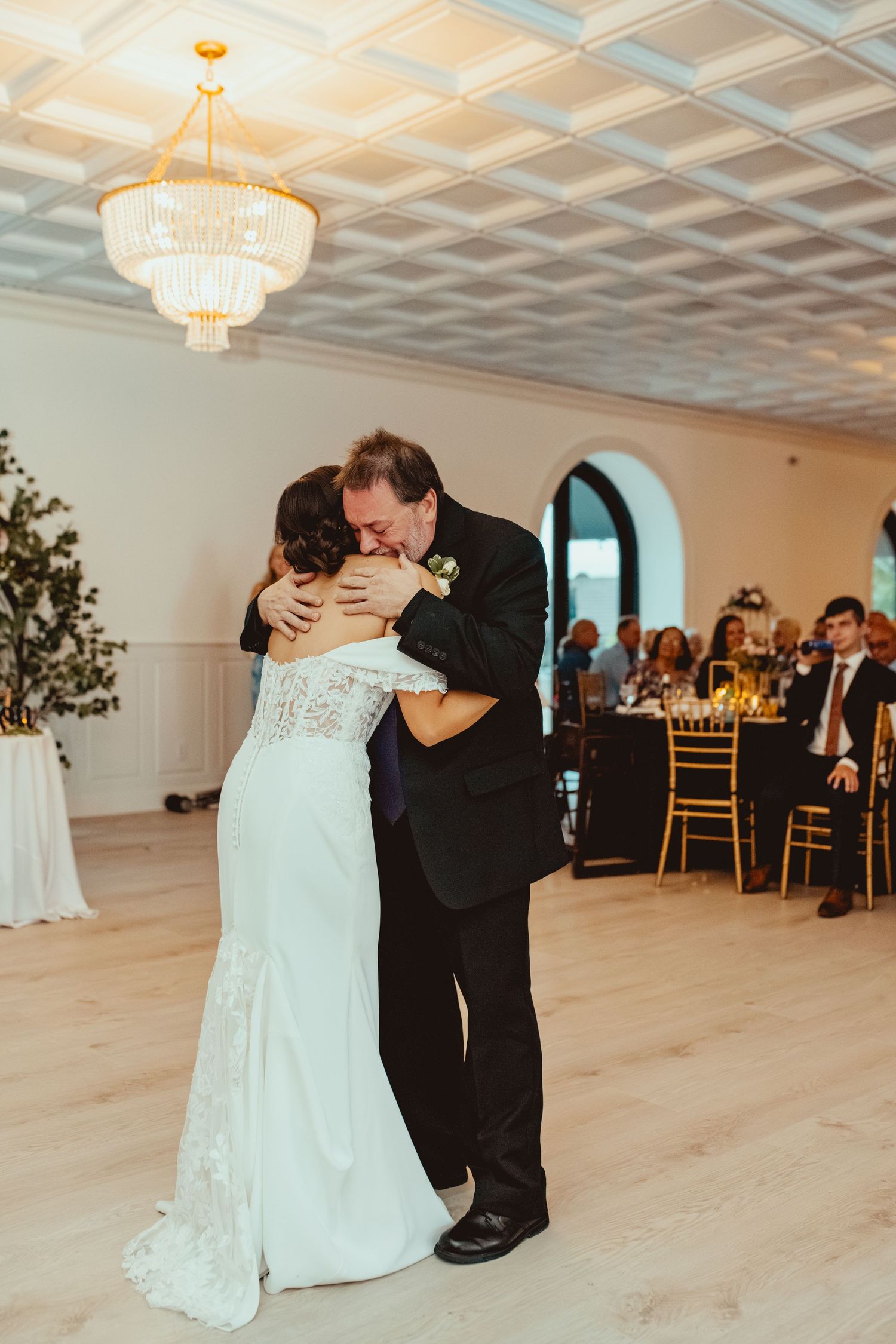 A tender moment during a wedding reception as a couple embraces under an elegant crystal chandelier.