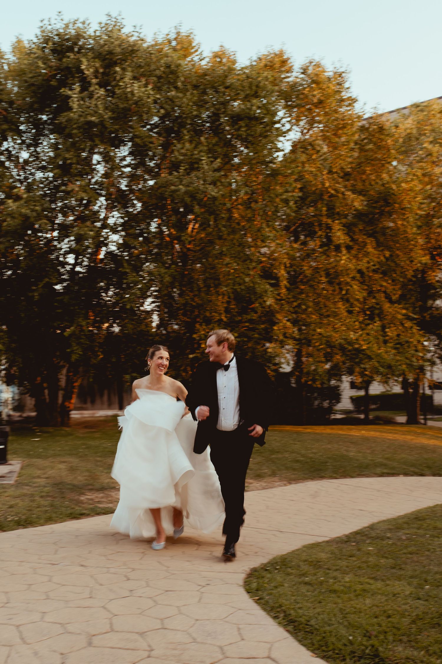 A couple runs playfully along an autumn path during their wedding photoshoot.