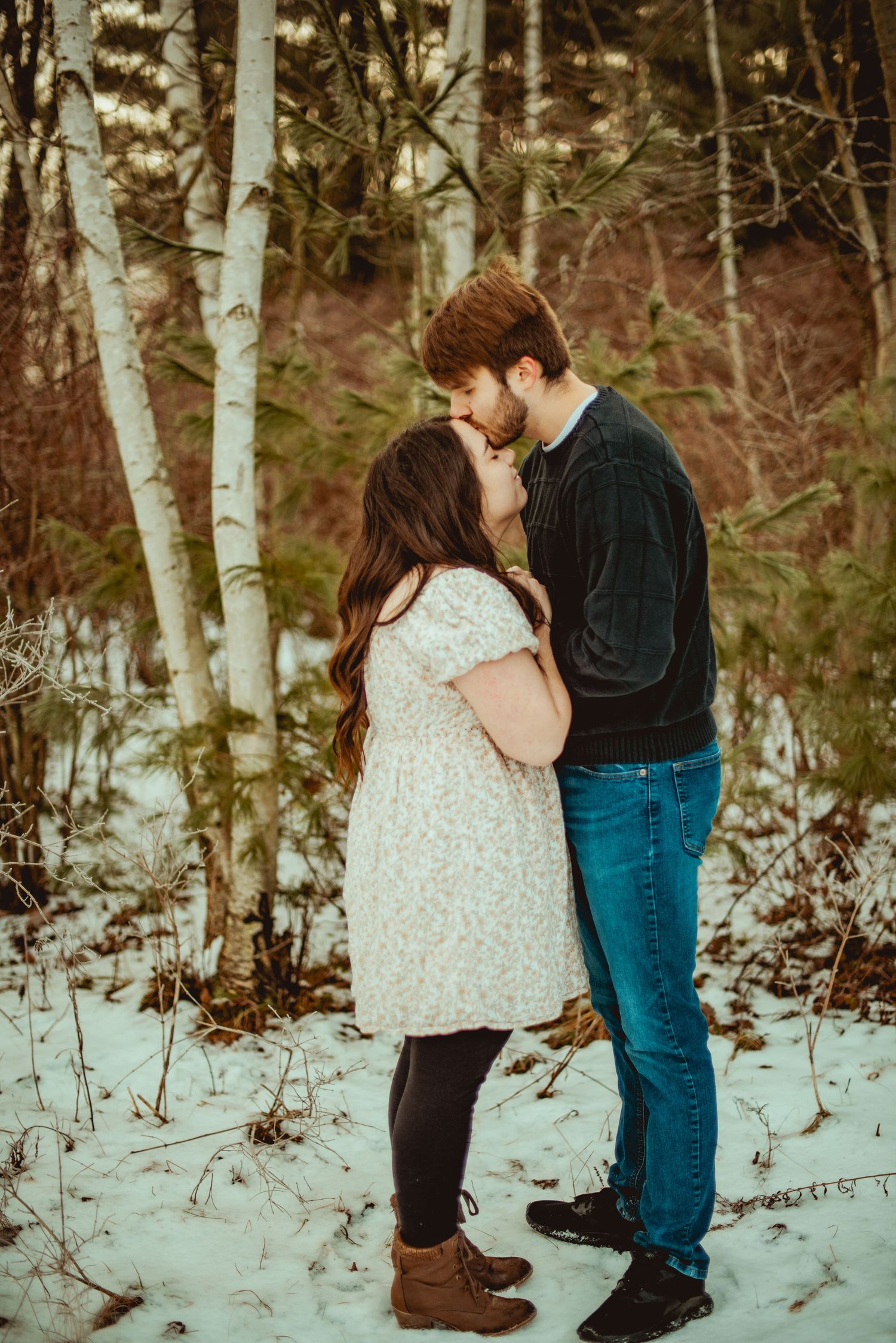 A romantic winter moment between a couple standing in snow among birch trees.