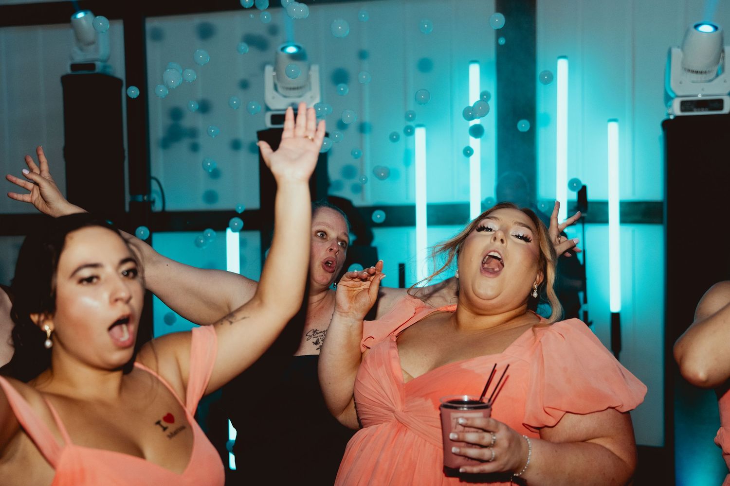 Bridesmaids in coral dresses dancing and celebrating at lively wedding reception party.