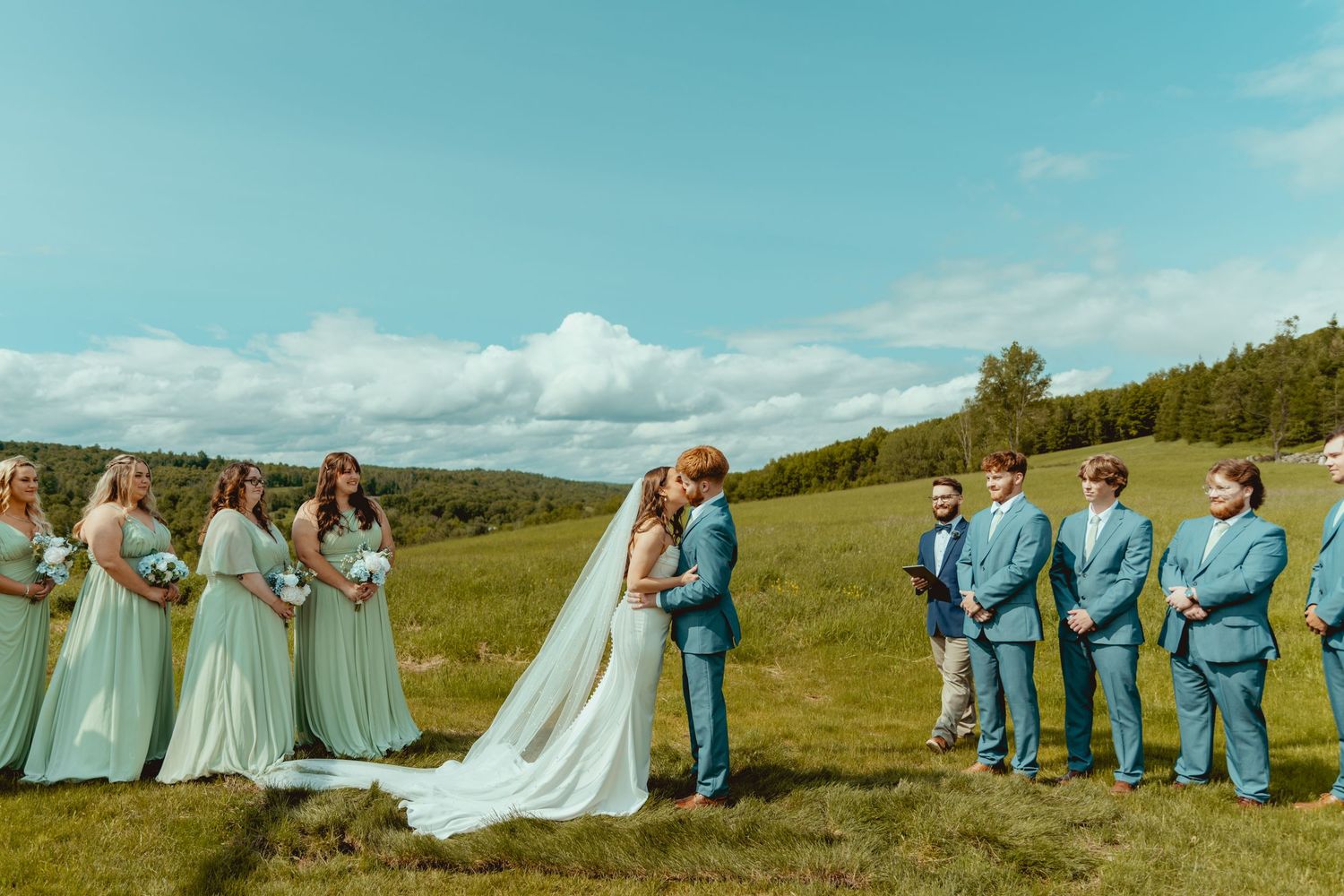 Wedding party in blue and white poses across a scenic mountain landscape.