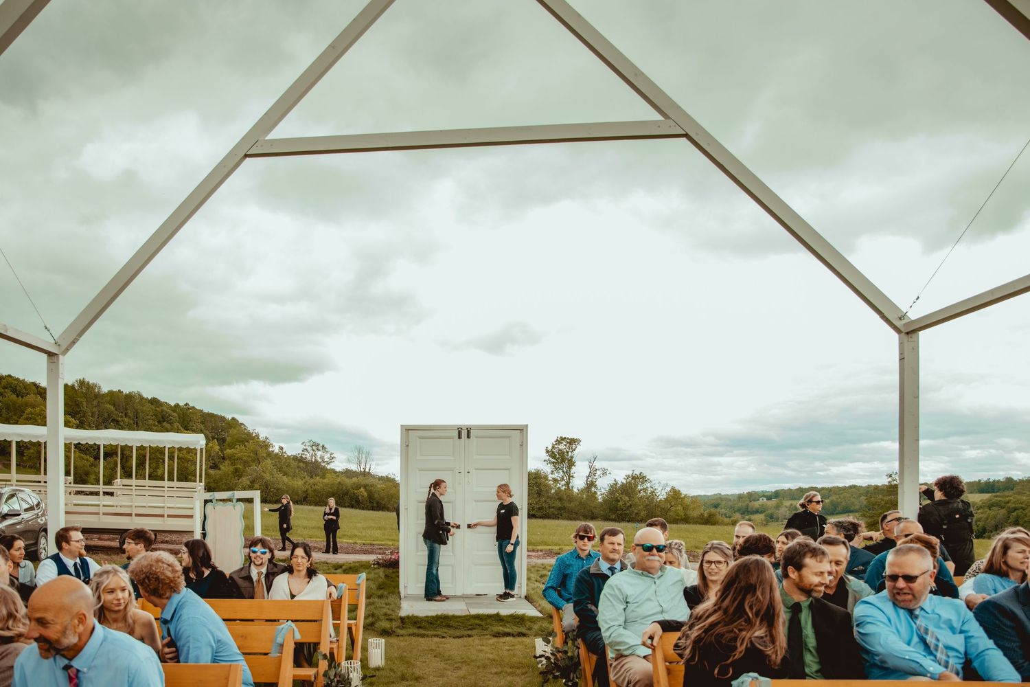 Modern outdoor wedding ceremony setup with white chairs arranged on grass under an overcast sky.