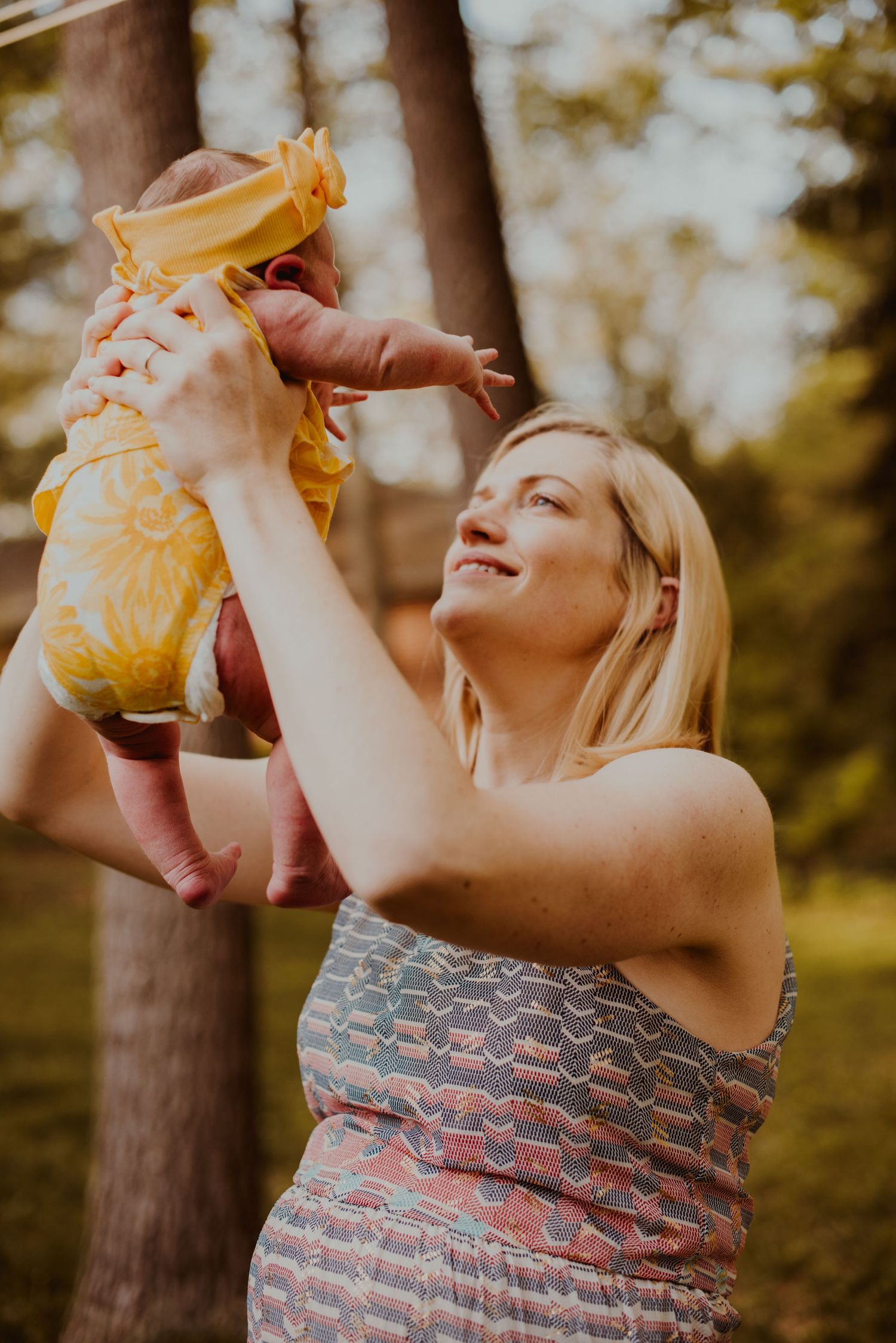 A joyful maternity moment captured outdoors with sunlight filtering through trees in the background.