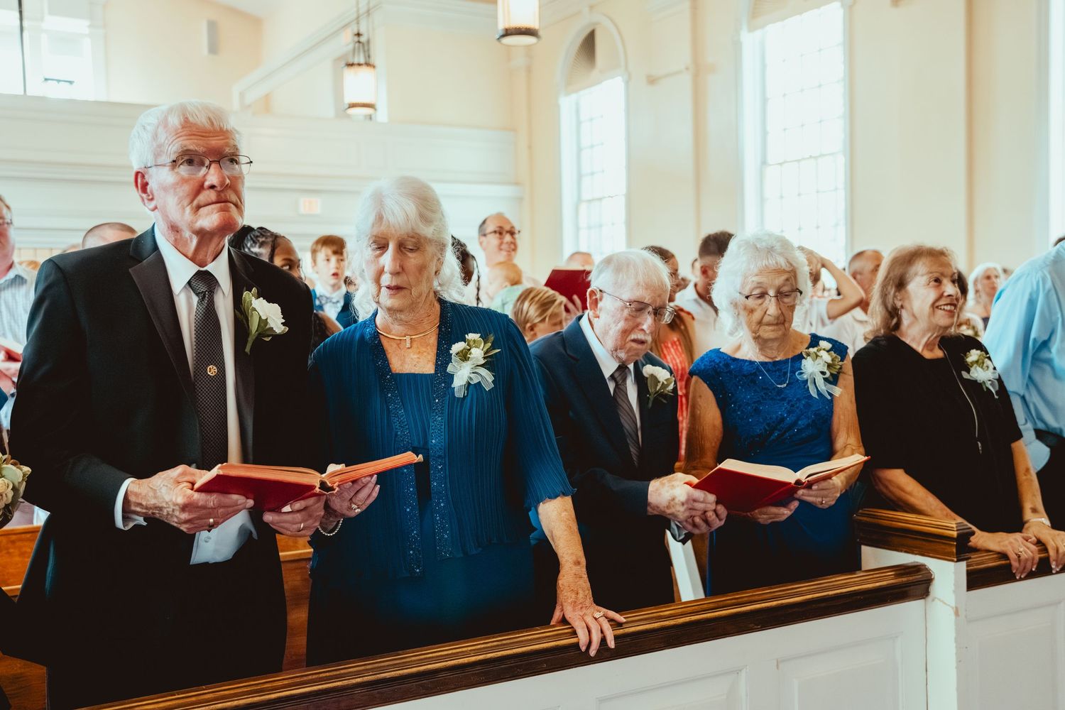 Wedding guests seated in church pews wearing formal attire in shades of blue and black.