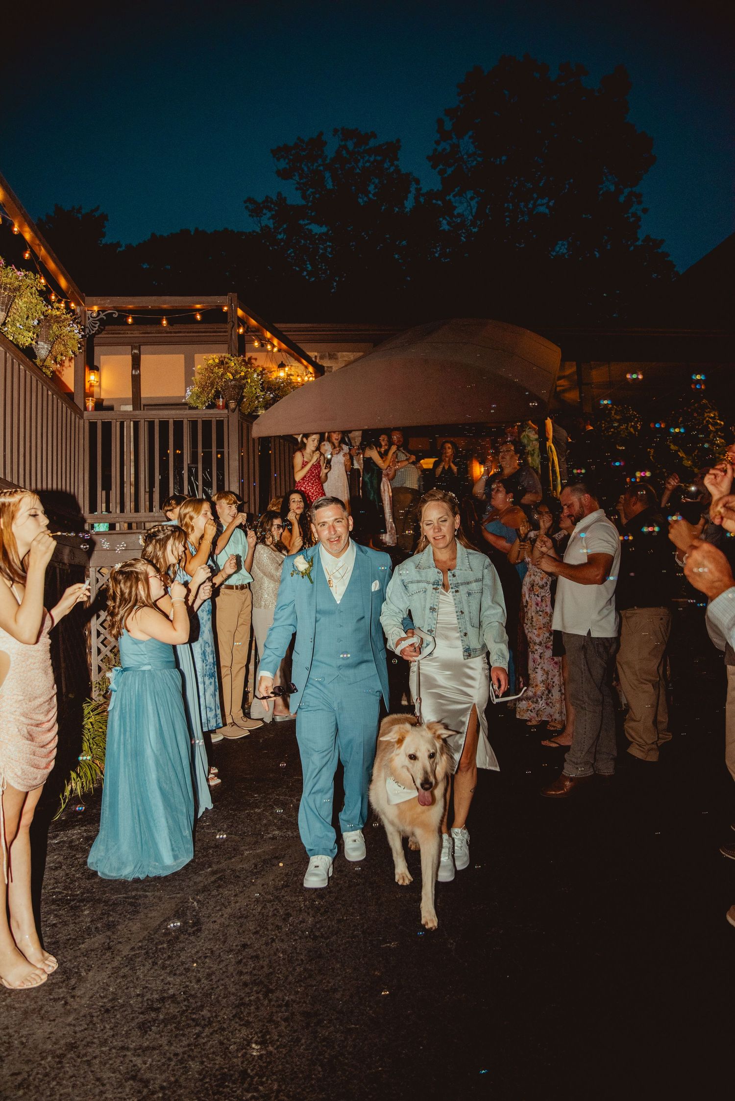 Wedding reception guests dancing and mingling outdoors at night under string lights.