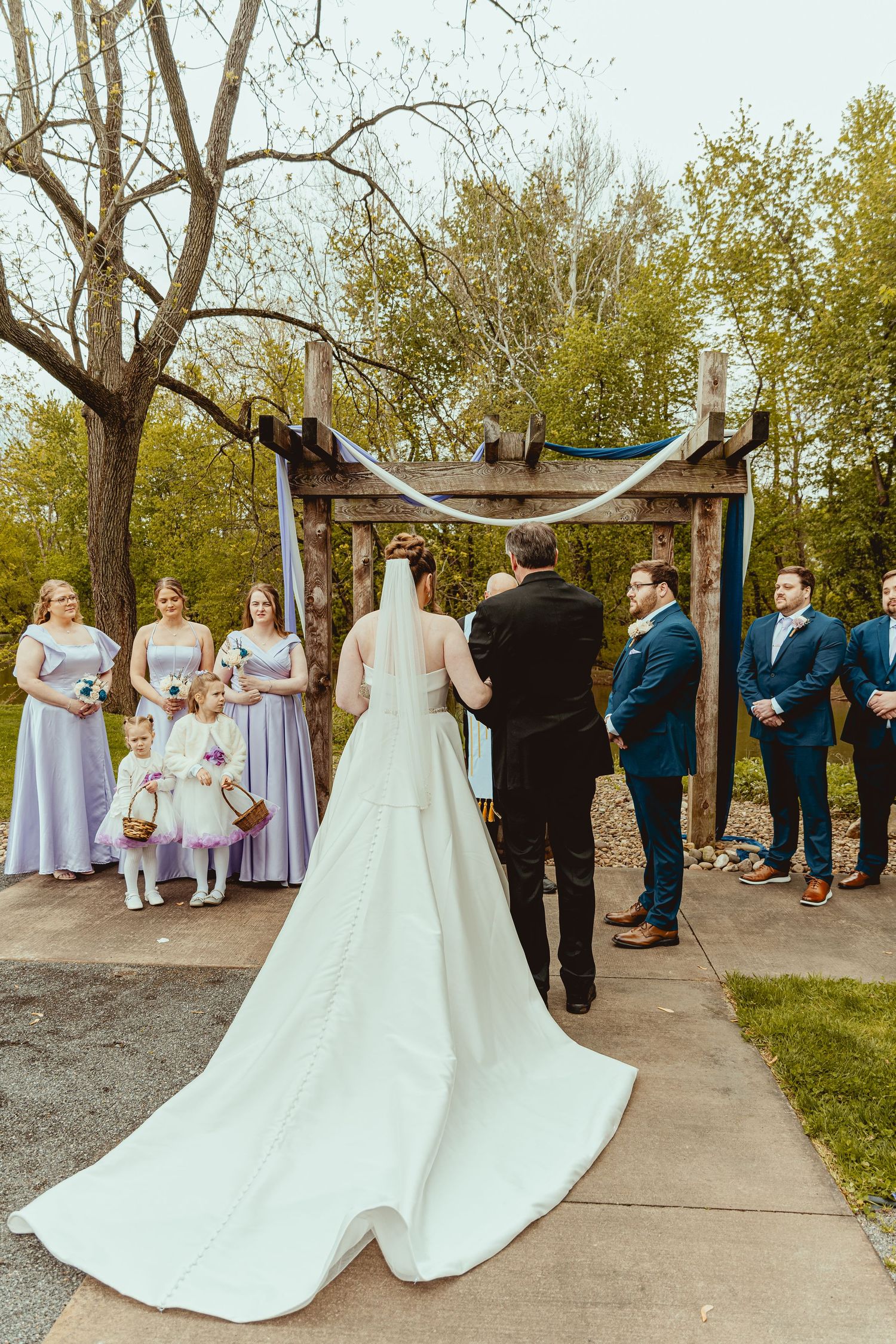 A bride and groom exchange vows at an outdoor rustic altar with bridesmaids in lavender and groomsmen in navy.