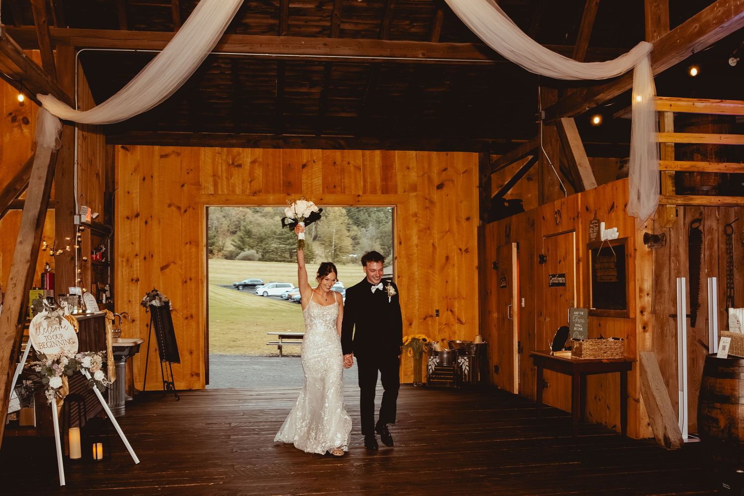 Newlyweds share their first dance in a rustic barn venue decorated with white draping and string lights.