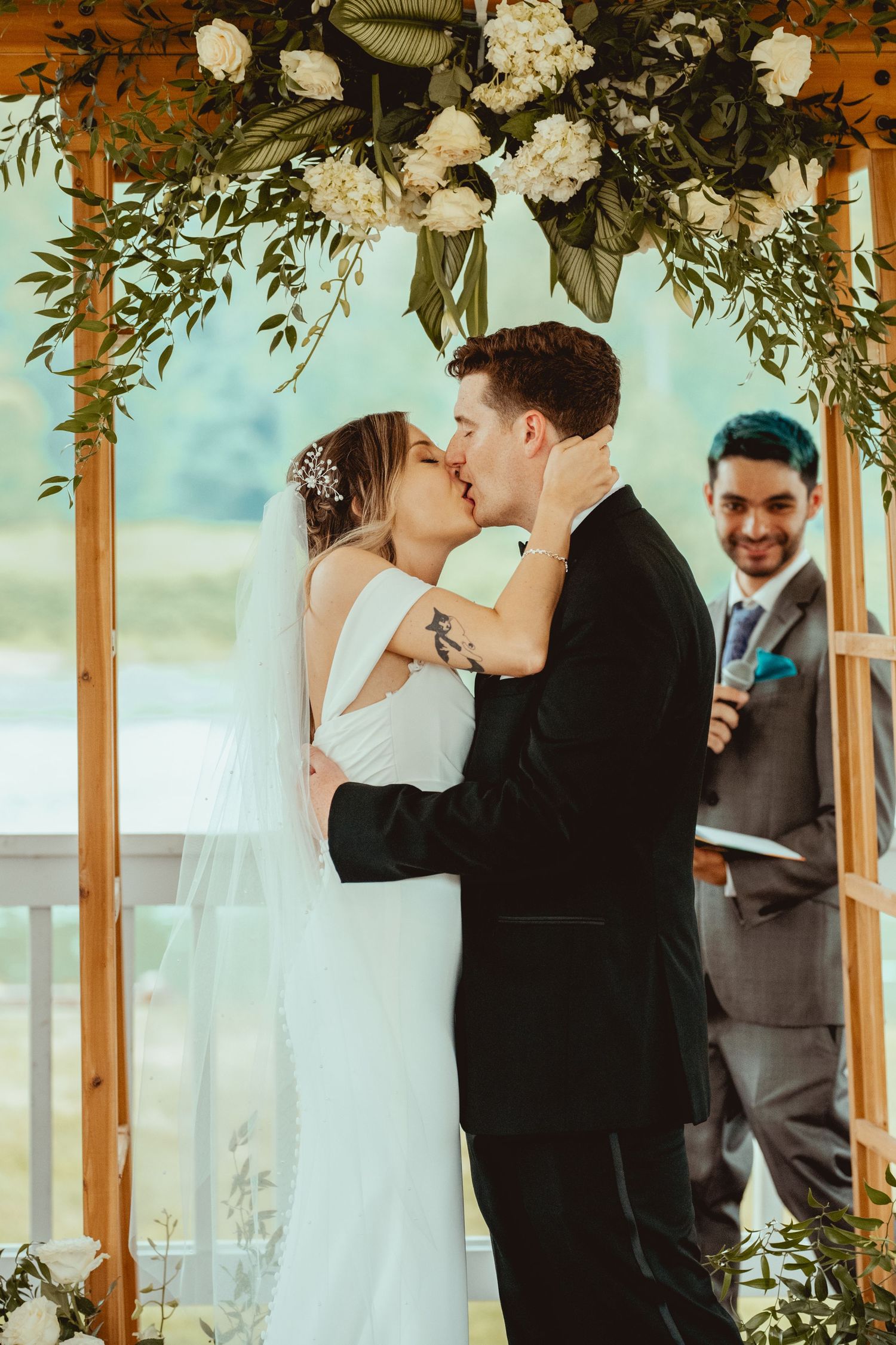 Wedding ceremony under a floral arch with white hydrangeas and greenery decorations.