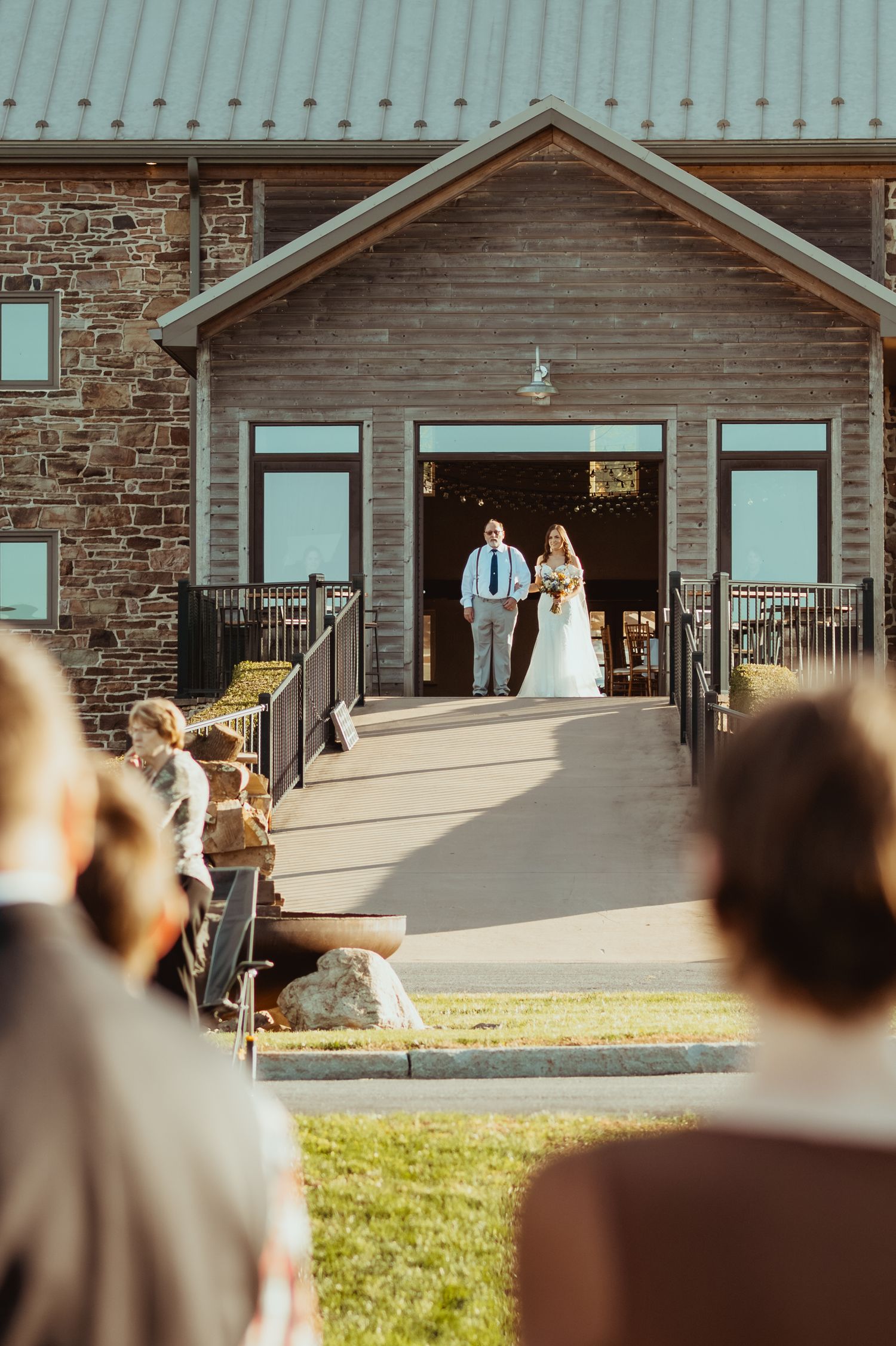 Wedding ceremony takes place at a rustic stone and wood venue with guests seated on the lawn.