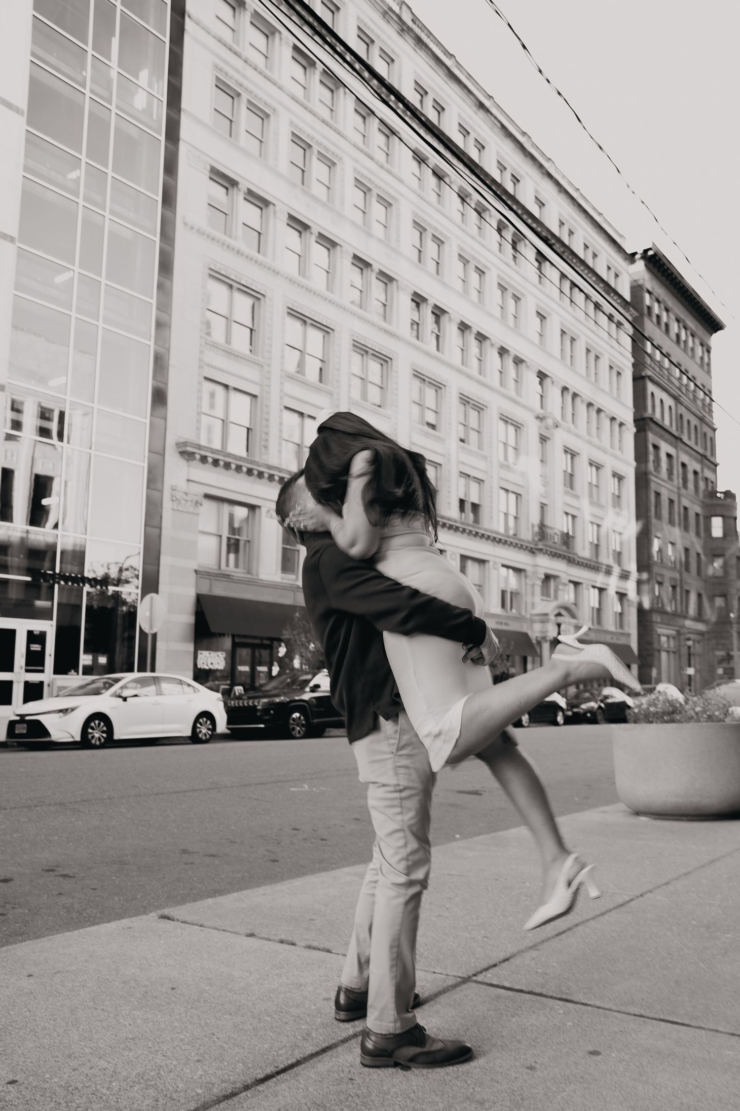 Black and white photos show playful poses on an urban sidewalk near a modern building facade.