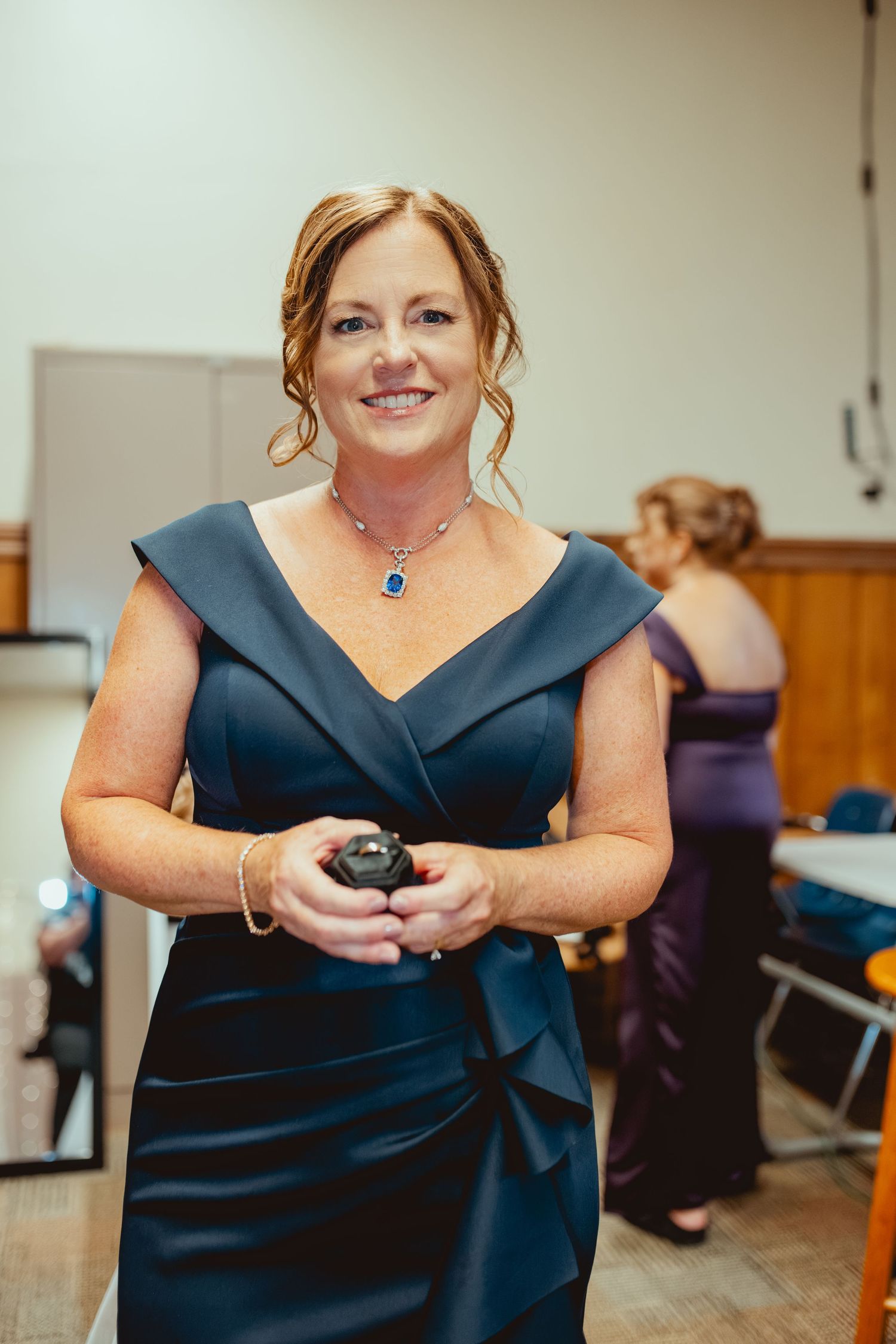 Person in navy blue dress holding small items during wedding preparation.