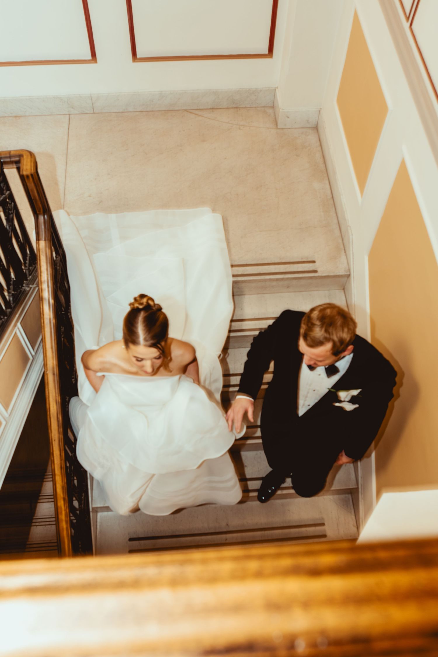 A couple descends an elegant staircase at their wedding, with the bride's white dress flowing behind them.
