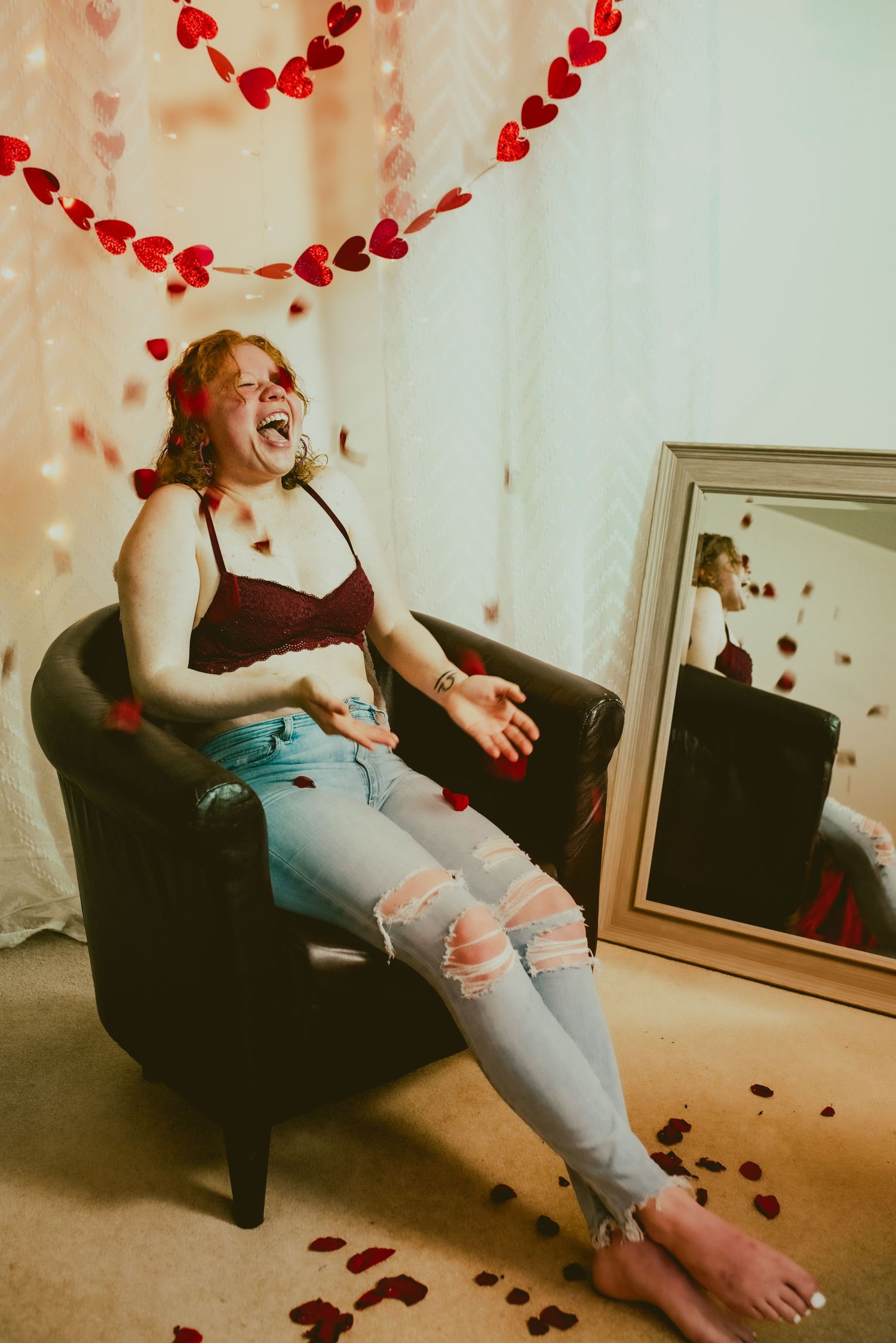 A person lounges on a couch laughing while red heart decorations float in the air around them.
