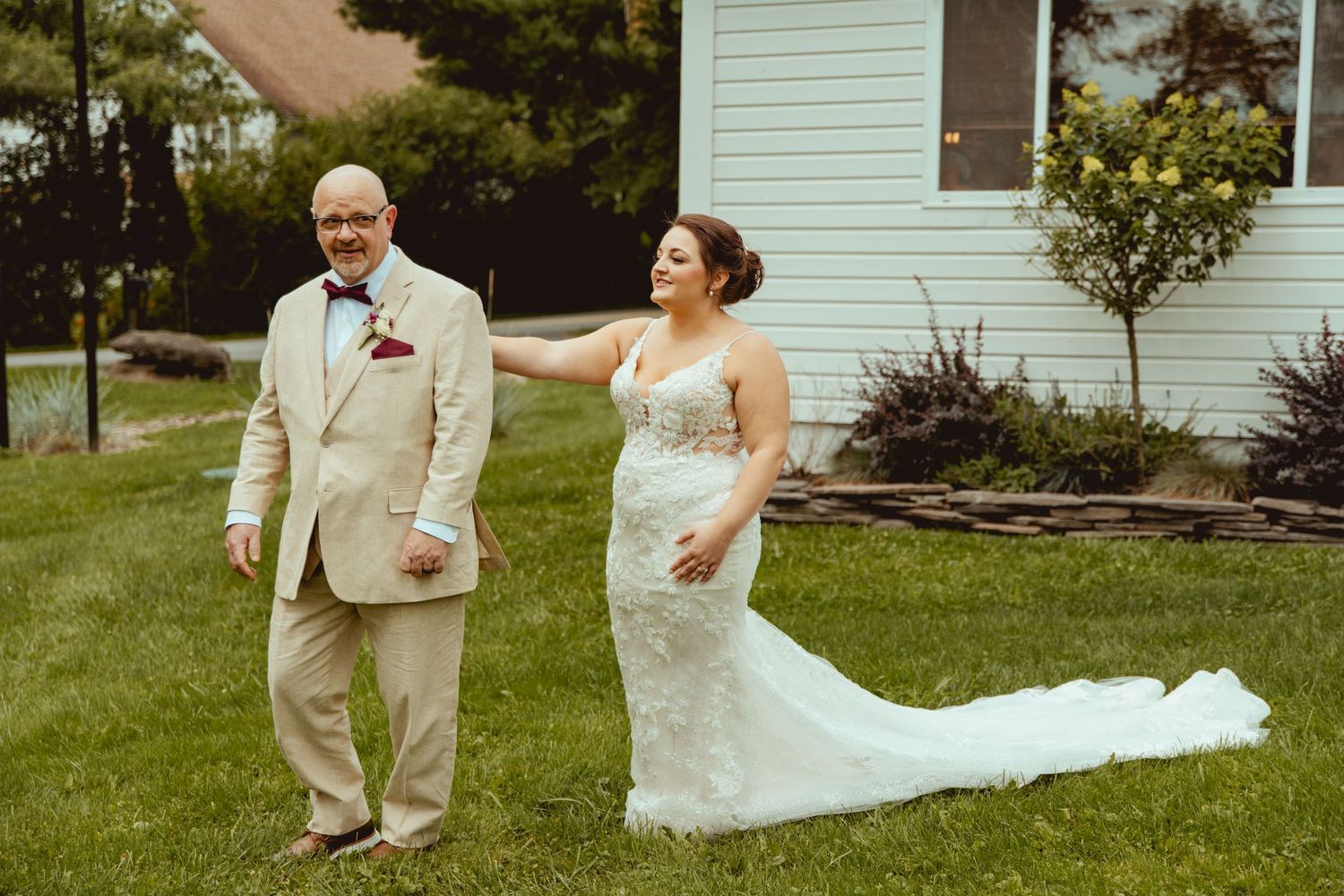 Bride in lace mermaid gown shares tender first look moment with father in tan suit.