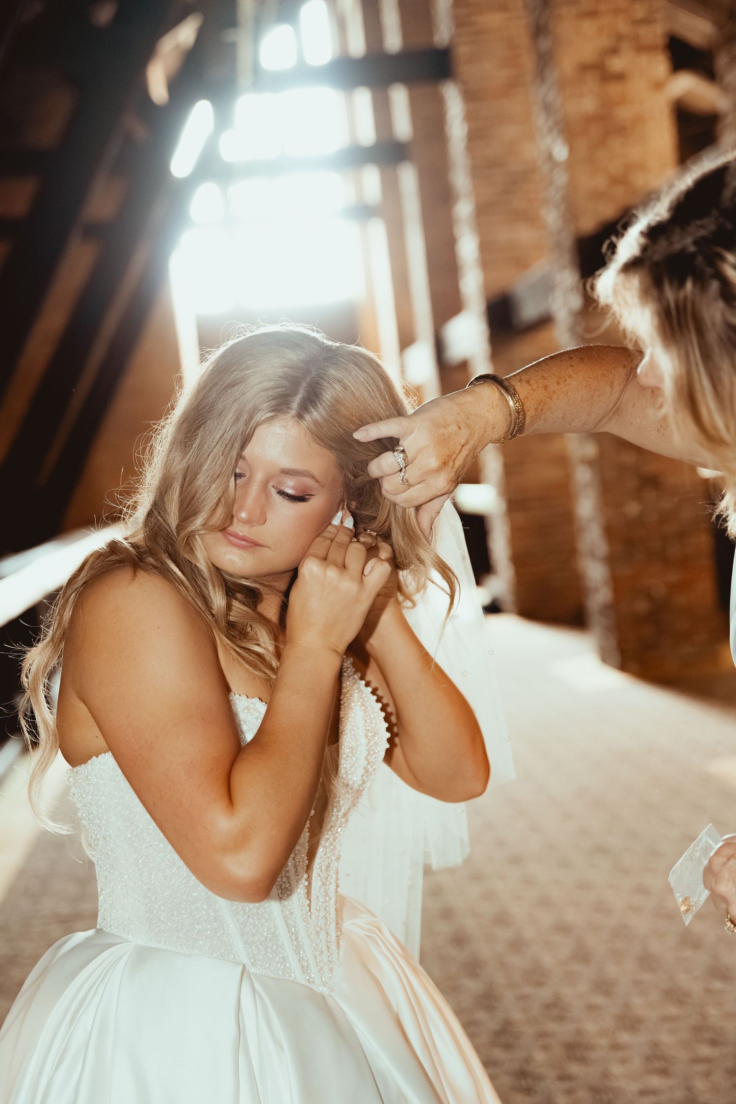 Bride putting on earrings with help from bridesmaid in rustic barn wedding preparation.