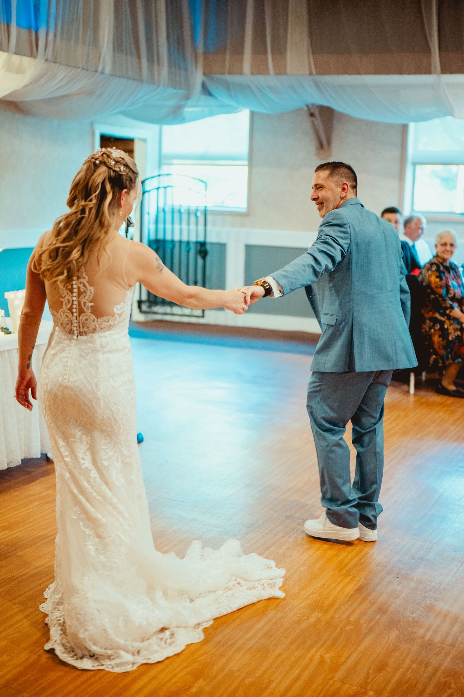 Wedding couple dancing playfully on hardwood floor at indoor reception venue.