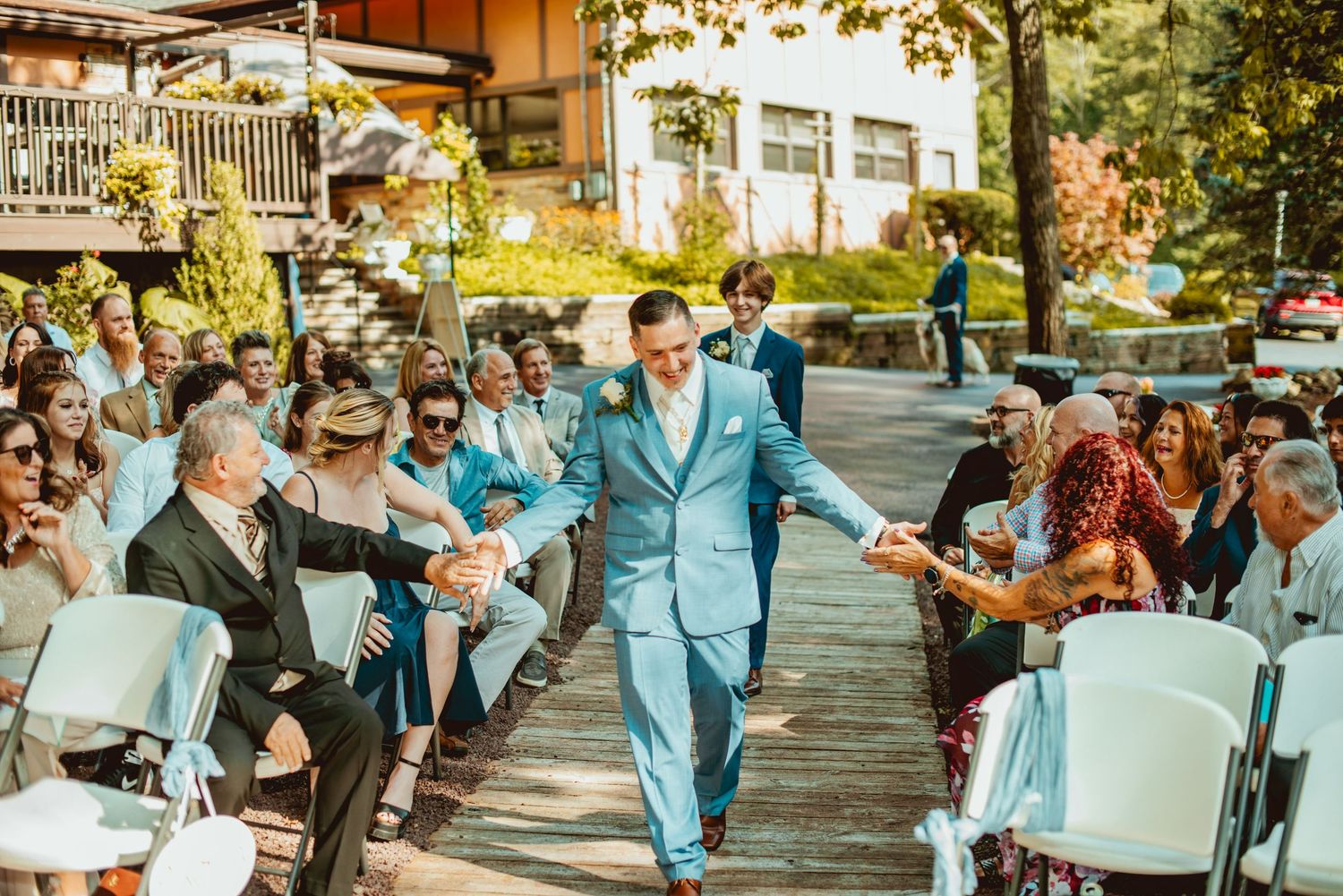 Wedding guests dance and celebrate together on an outdoor deck during a festive daytime reception.
