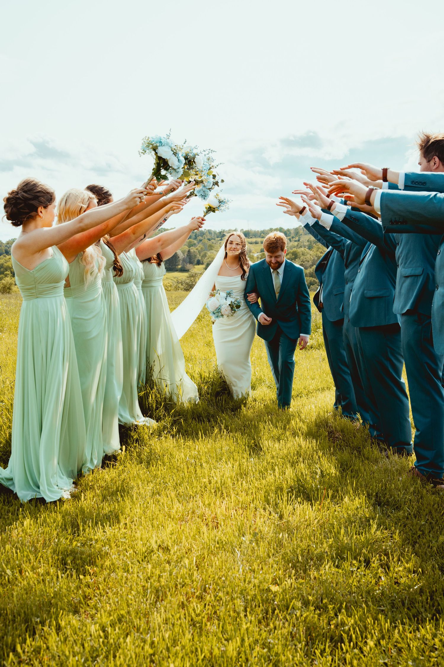 Wedding party in mint green dresses and navy suits posing in a sunny field.