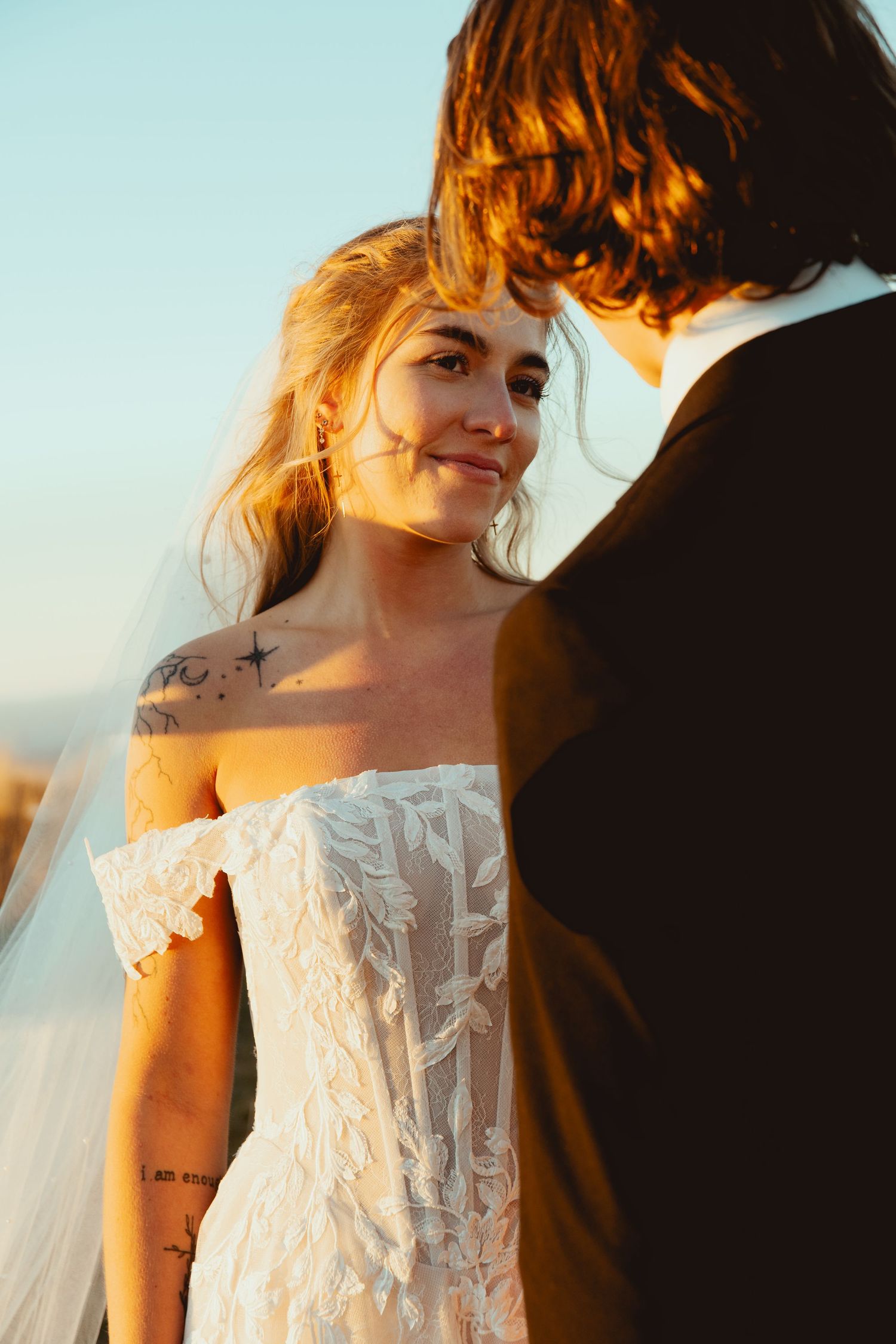 Couple in romantic golden hour lighting with one wearing a delicate white lace dress.