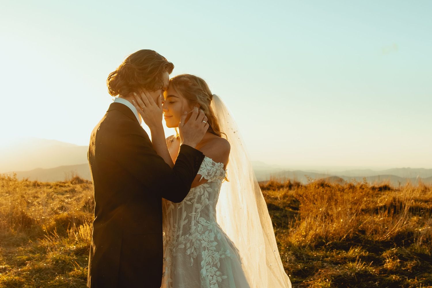 Romantic sunset silhouette of couple embracing in golden light against mountain landscape.
