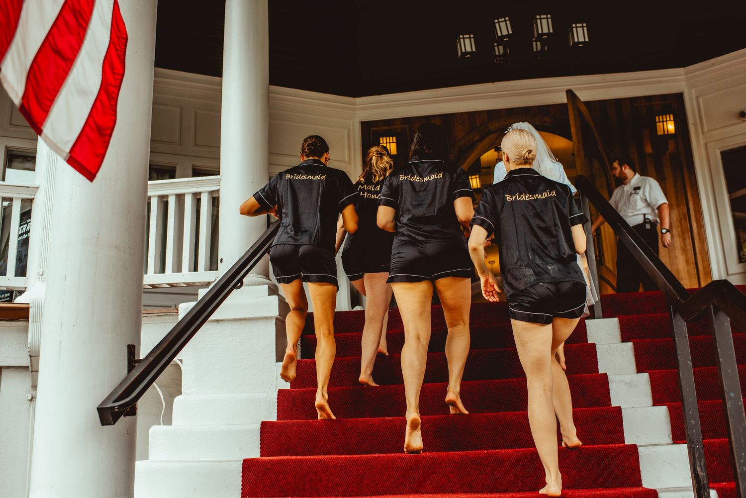 Wedding party members ascending red-carpeted stairs in formal attire.