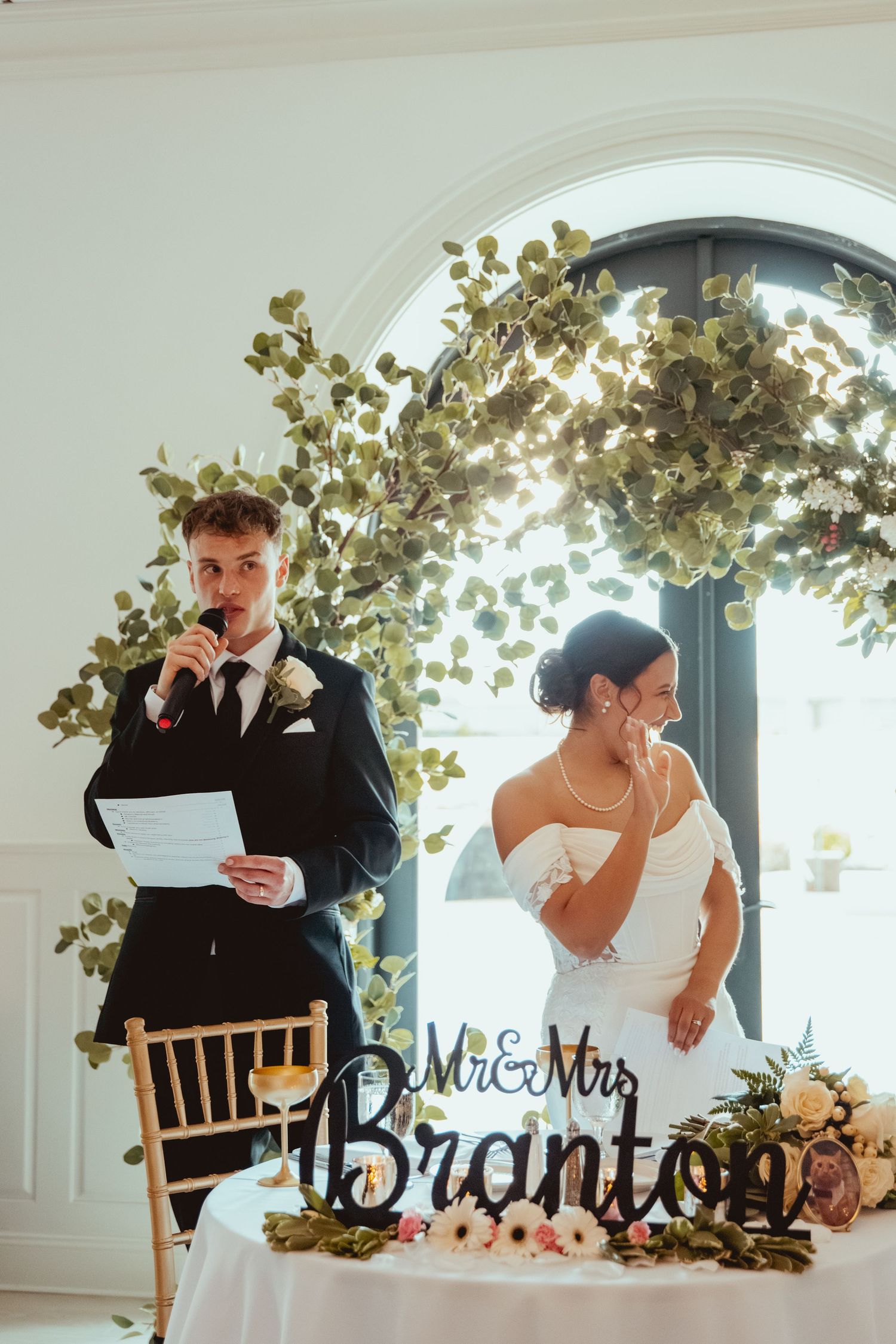 Wedding reception table with Mr and Mrs sign decorated with greenery and elegant place settings.