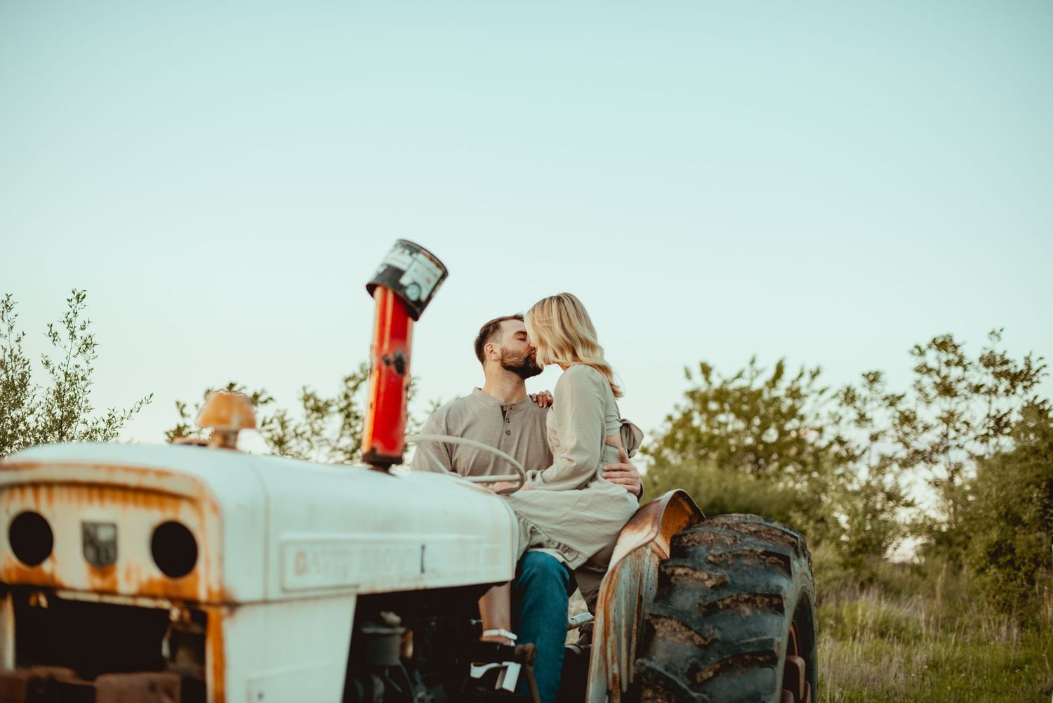 Two people share a playful moment on a vintage blue pickup truck at sunset.