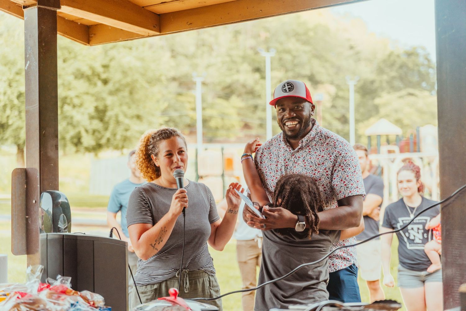 People gather at a covered outdoor venue, sharing food and drinks while socializing at picnic tables.