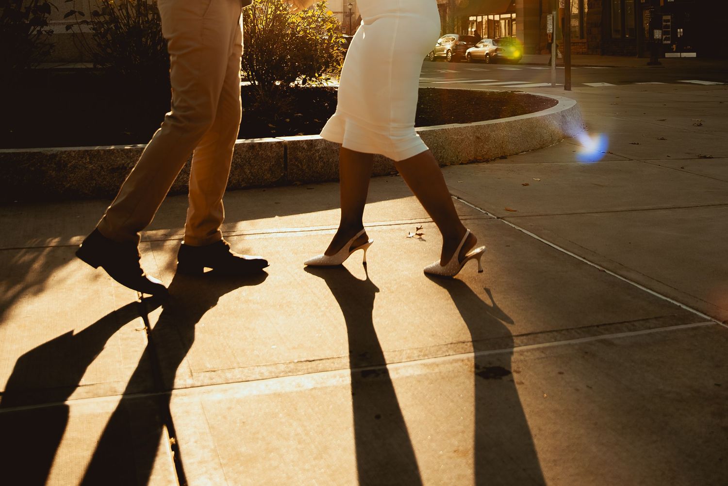 Silhouettes of people walking cast long shadows on an illuminated sidewalk at night.
