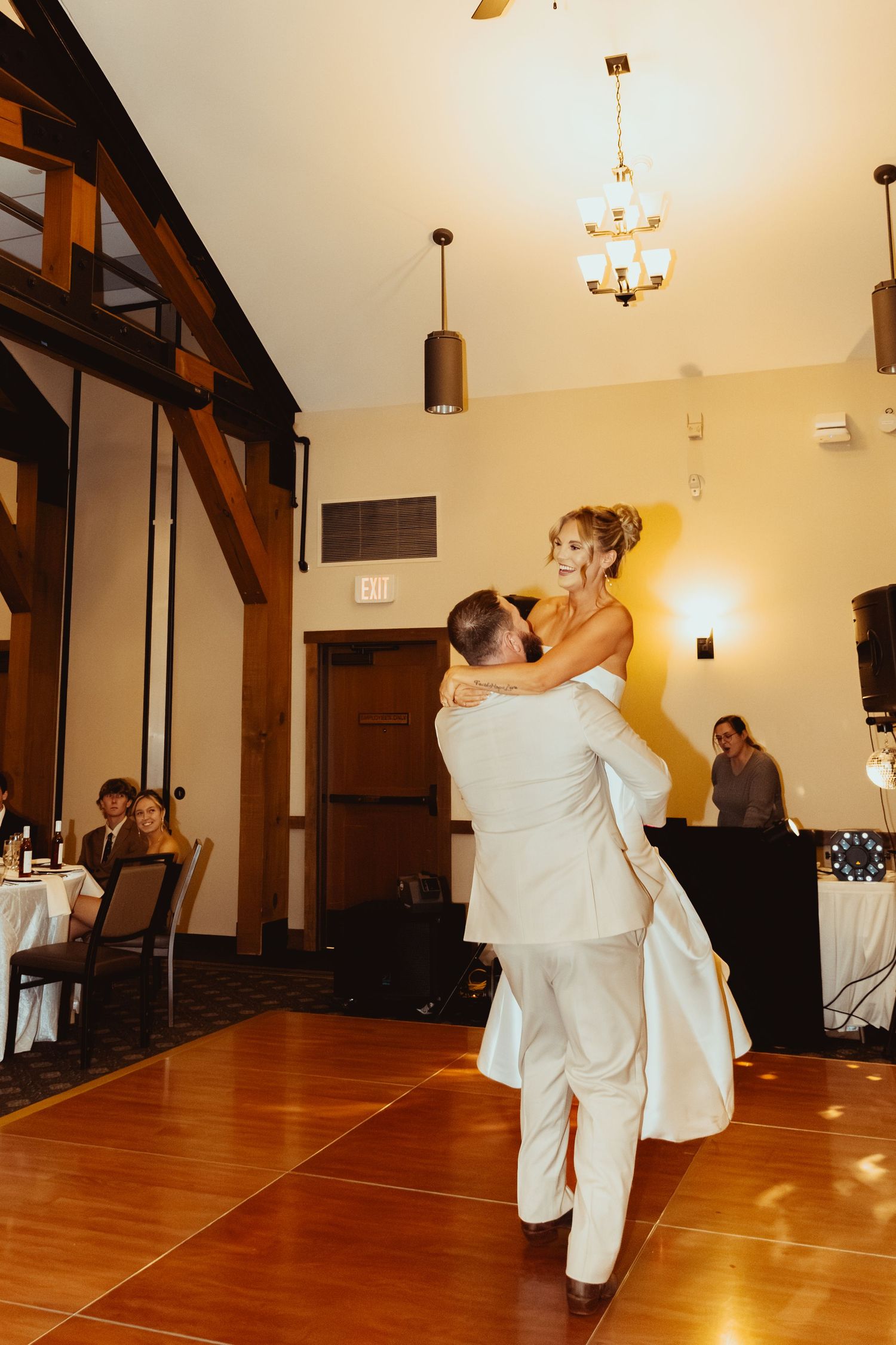 A couple in white attire performs an elegant dance move on a polished wooden floor in an elegant venue.
