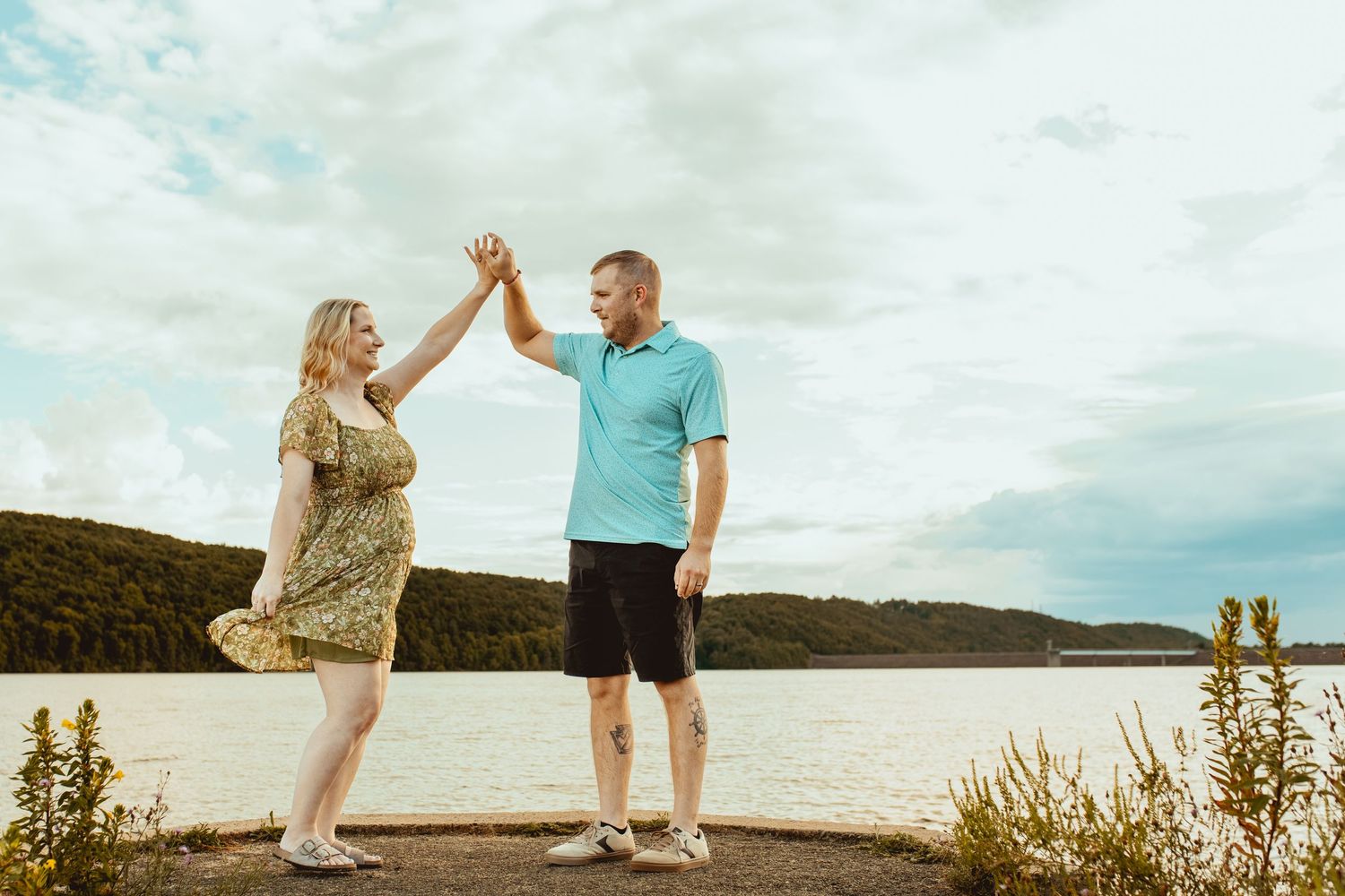 A couple stands together against a scenic mountain landscape during sunset, giving each other a high five.