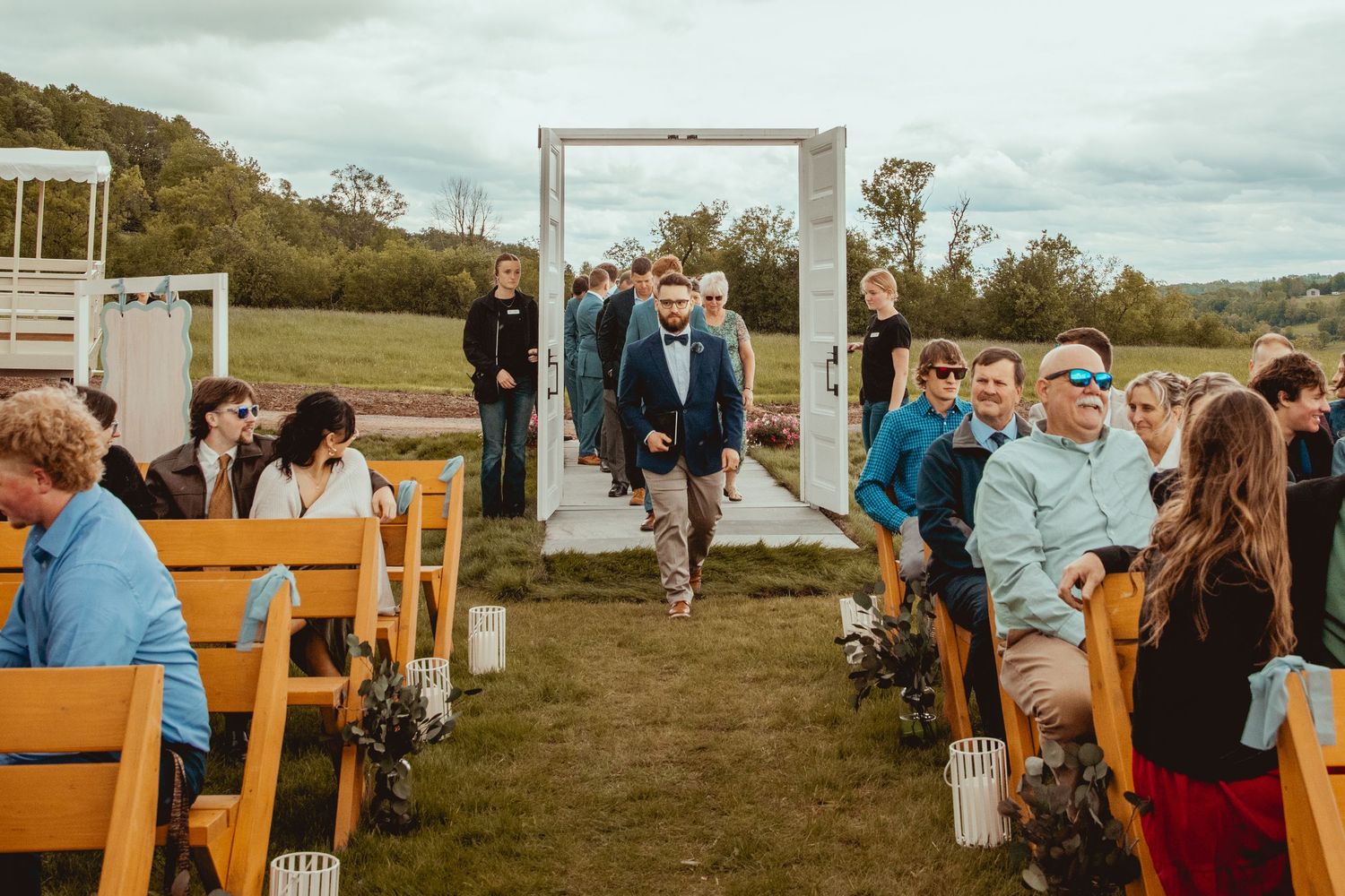 Wooden benches set up for an outdoor wedding ceremony with a white arch in the distance.