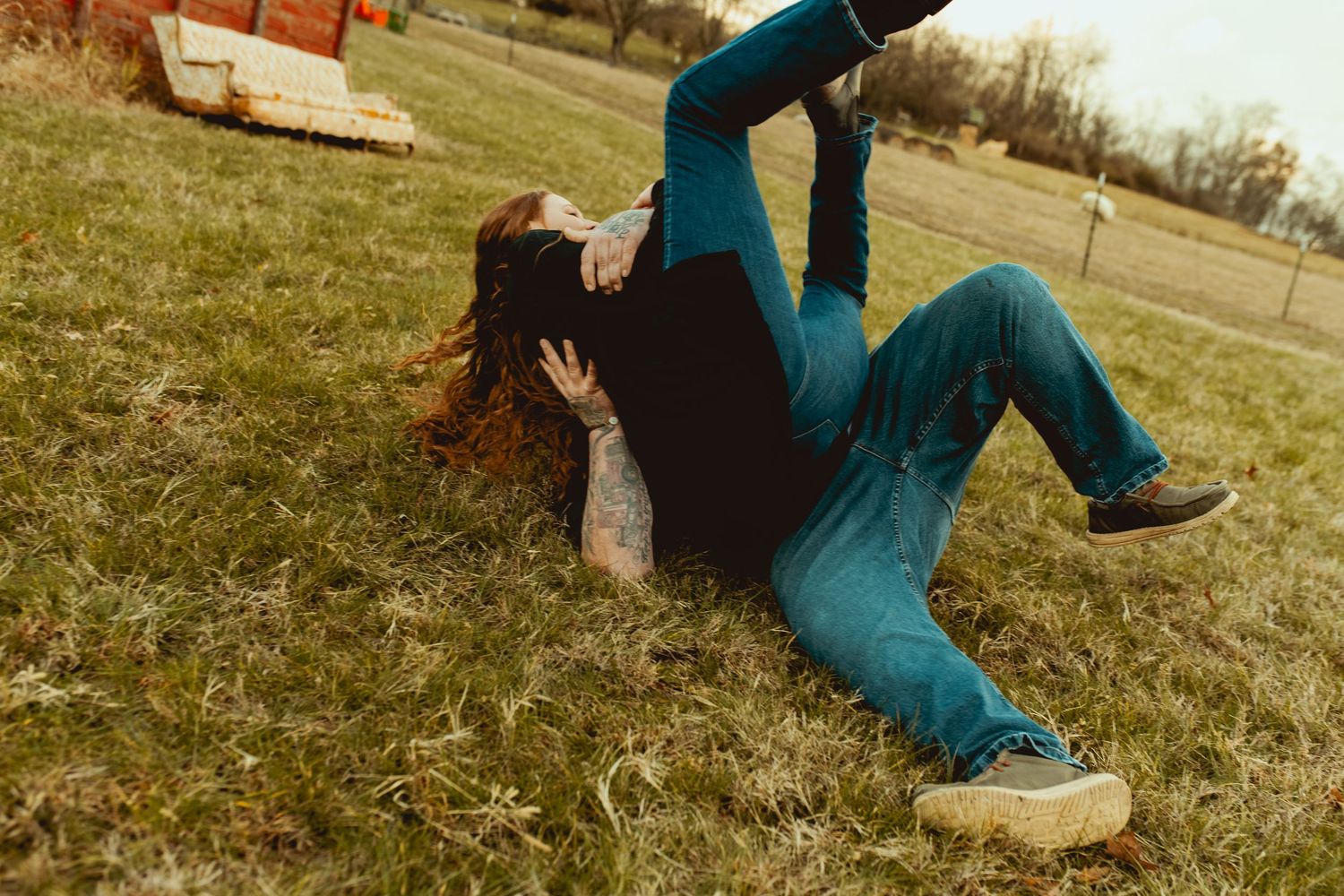 Someone in a blue jumpsuit falls backwards onto grass in a playful pose during an outdoor photoshoot.