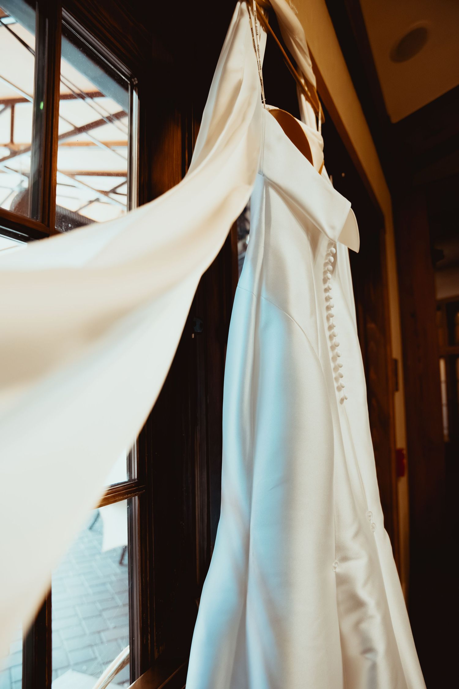 A row of elegant white wedding dresses with button details hanging on dark wooden hangers in a bridal shop.