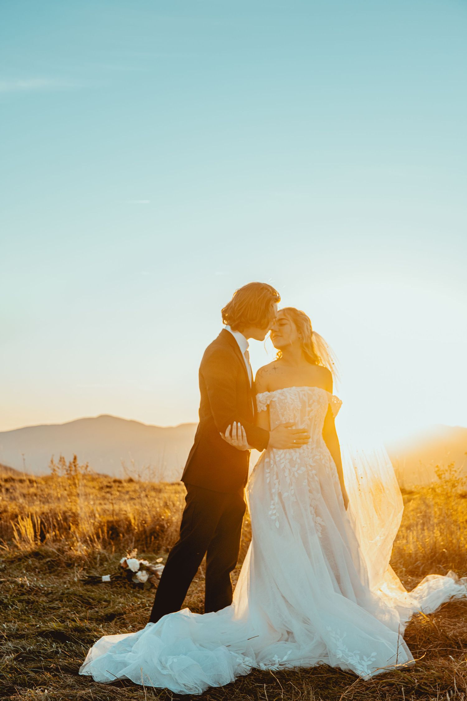 A wedding couple shares an intimate moment against a mountain landscape at sunset.