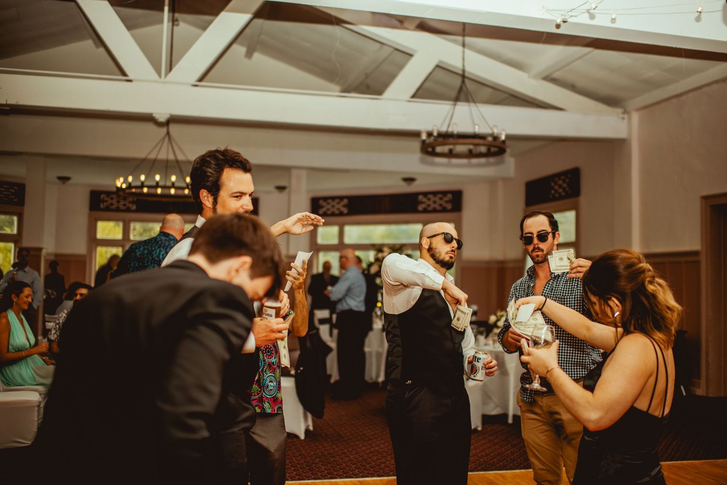 Wedding guests dancing and celebrating in a reception hall with exposed beam ceilings.