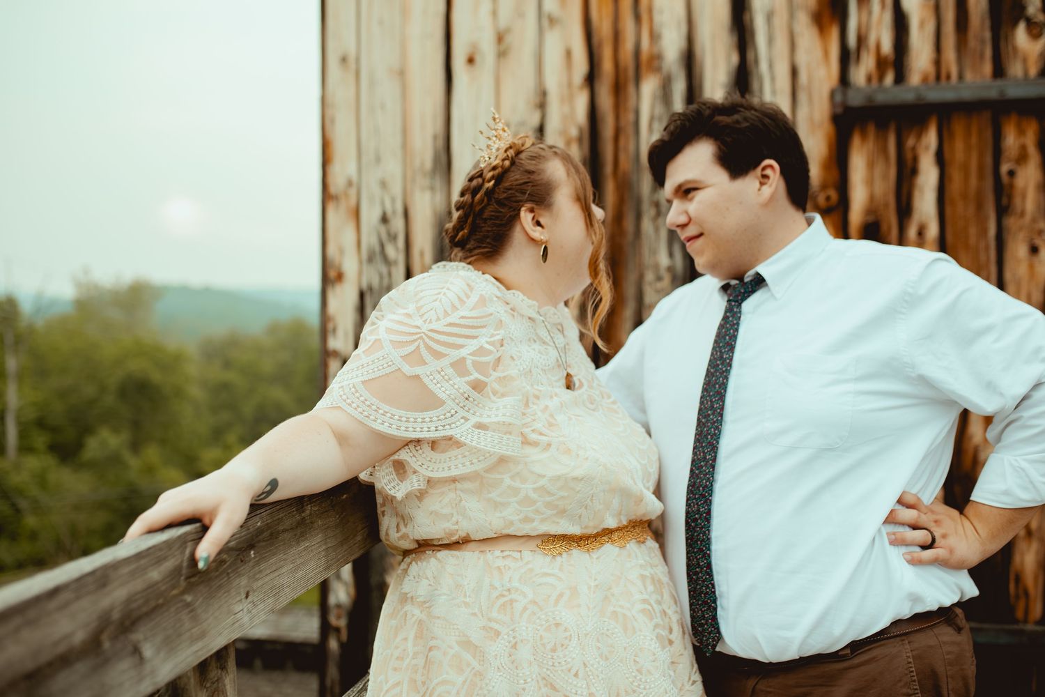 A couple in wedding attire share an intimate moment against a rustic wooden barn backdrop.