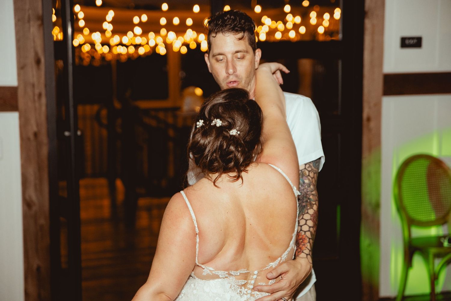Bride and groom sharing their first dance under warm string lights in a rustic wedding venue.