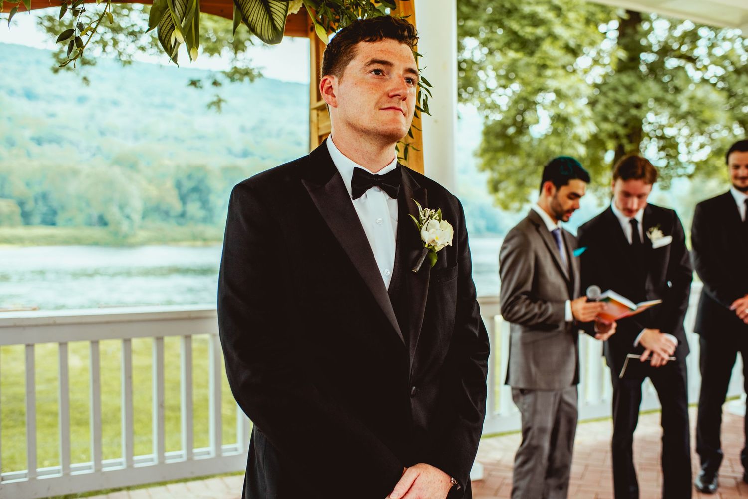 Wedding party members in formal attire stand together on an outdoor porch during a celebration.
