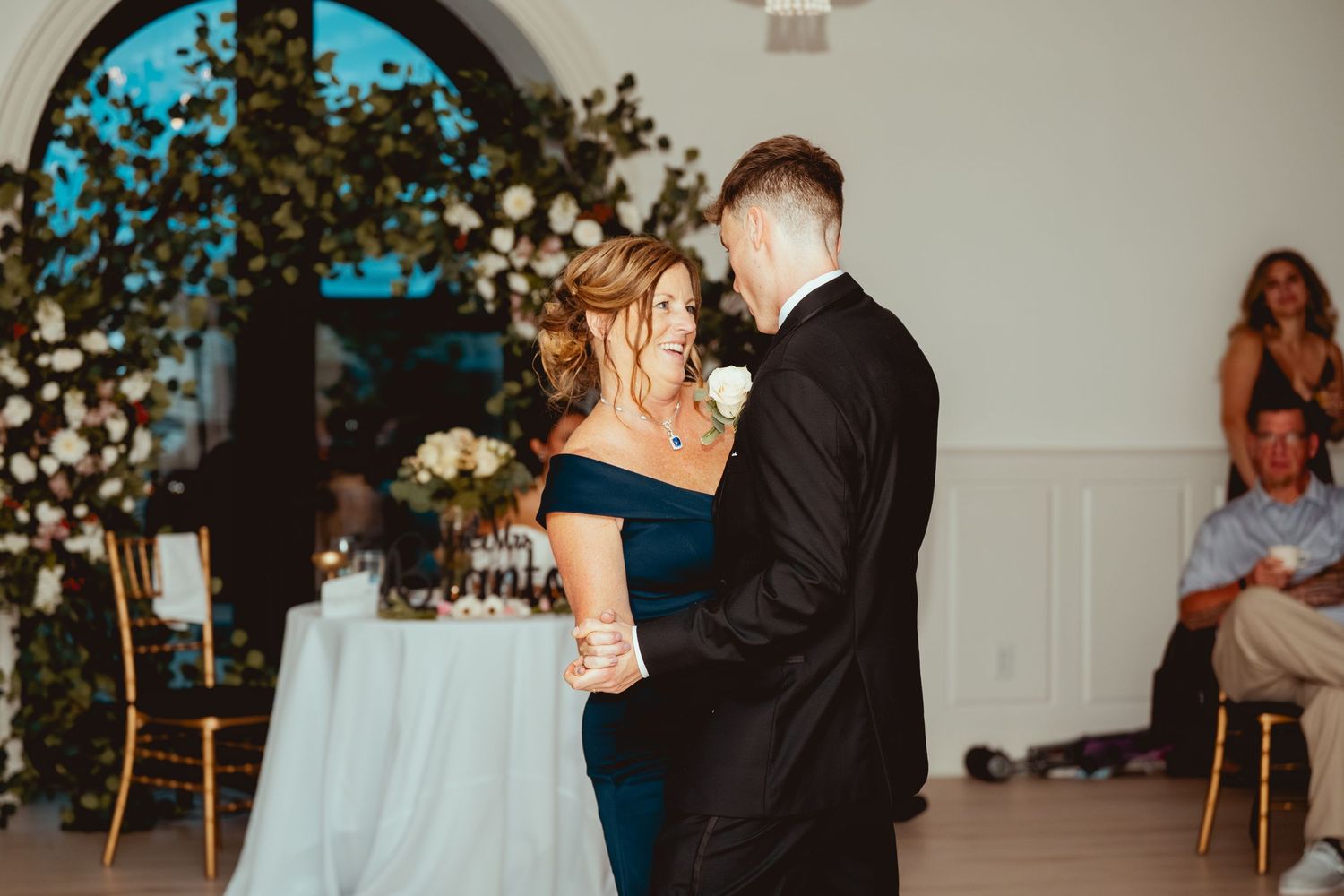 Wedding couple and guests during reception in an elegant white room with arched windows.